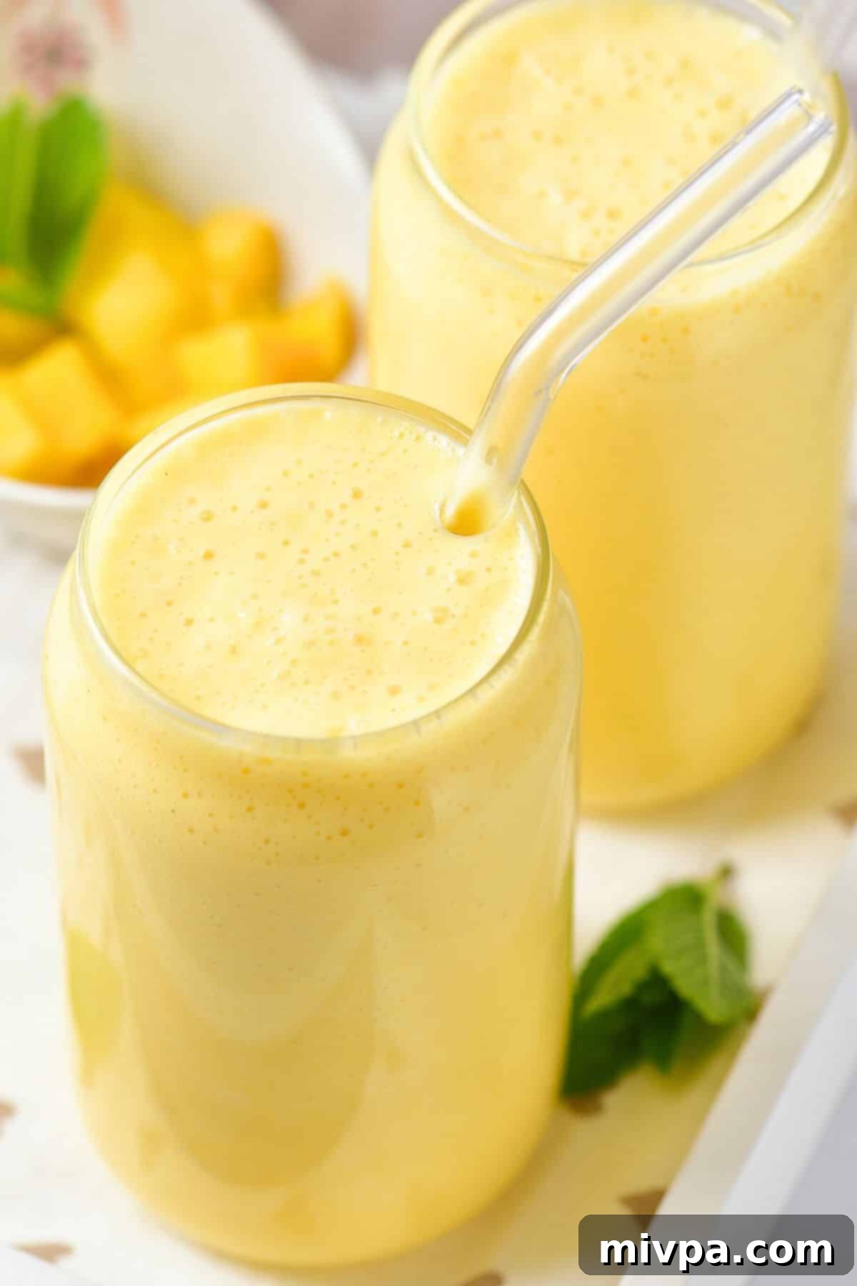 Fresh mango milkshake Up close shot of a glass of mango milkshake, garnished with mint and a few mango pieces, looking incredibly fresh and inviting.