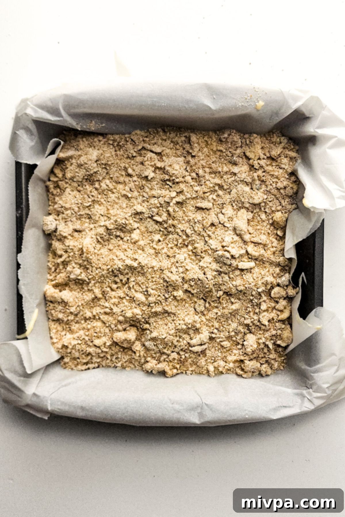 Easy Gluten-Free Crumb Cake with Streusel Topping Layer The first layer of streusel topping scattered over the cake batter in a parchment-lined cake pan, ready for more batter.