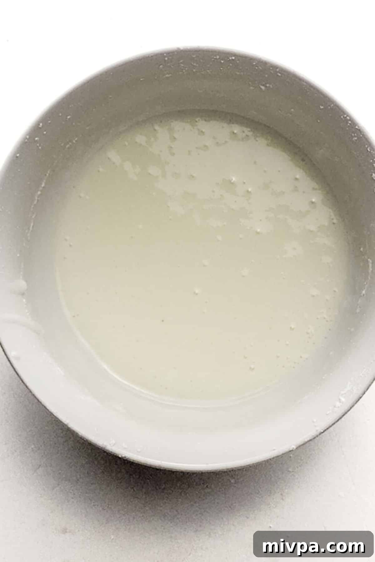 Crumb Cake Glaze Preparation A simple white glaze mixture in a small white bowl, whisked to a smooth, pourable consistency.