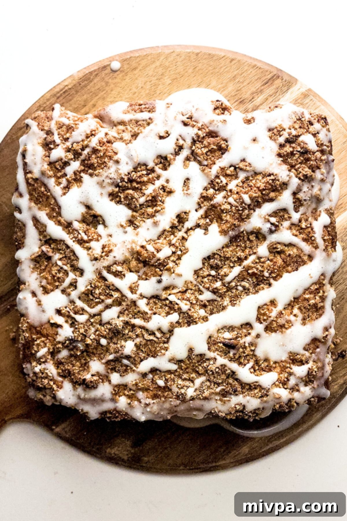 Easy Gluten-Free Crumb Cake Recipe with Glaze White glaze being artfully drizzled over the golden-brown crumb cake, adding a final touch of sweetness.