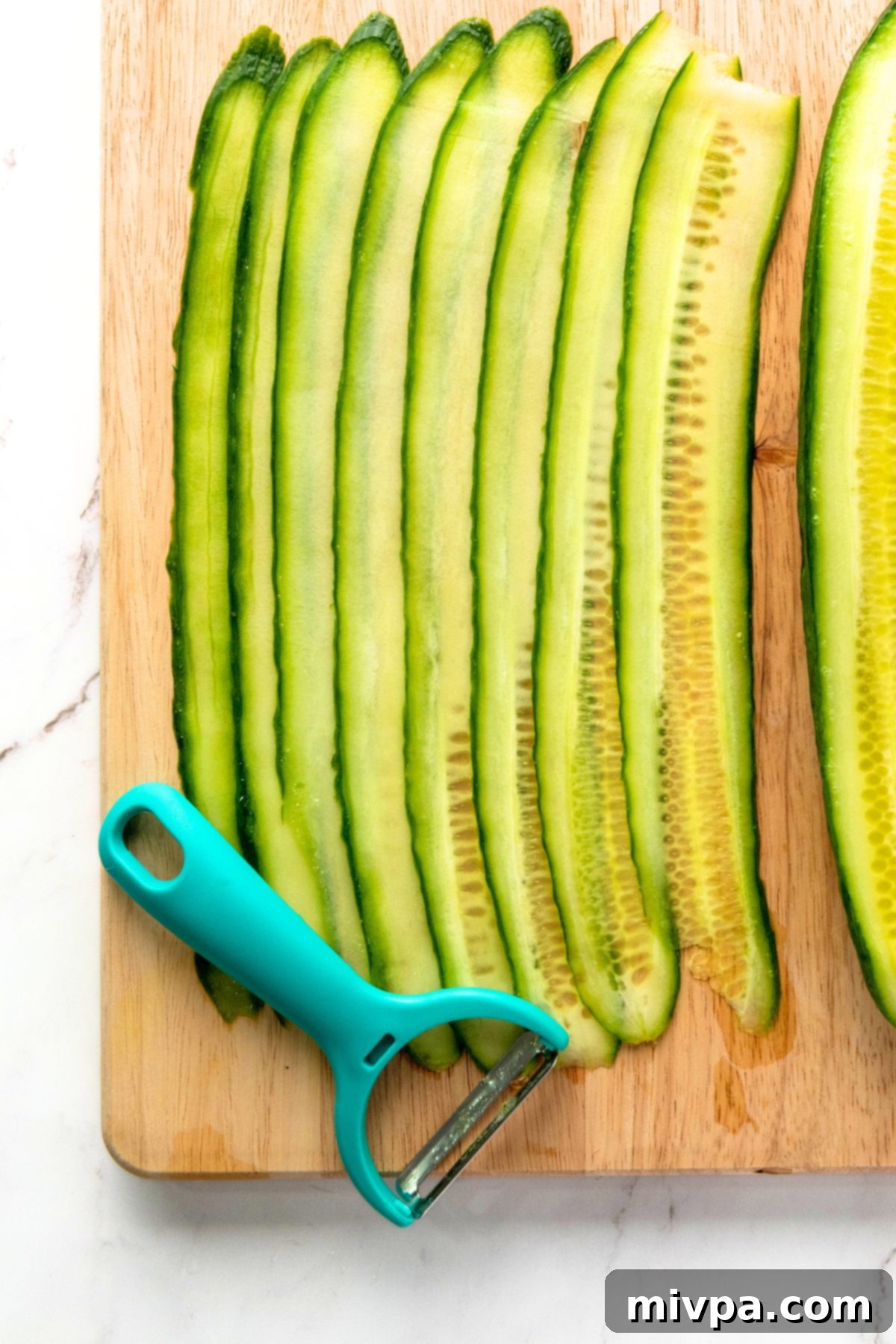Easy Cucumber Rolls with Cream Cheese Thin cucumber slices and vegetable peeler on wooden board.