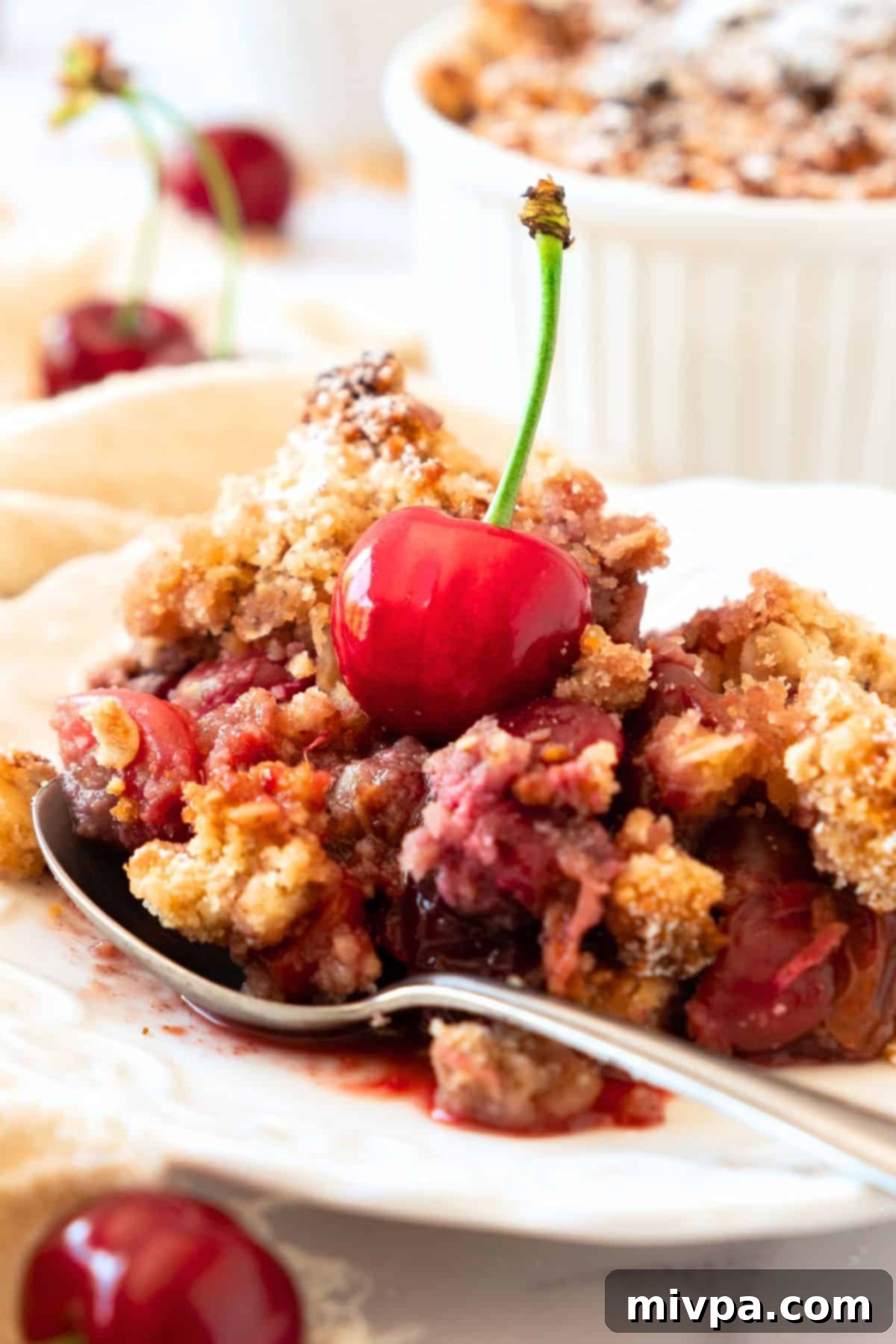 Easy Cherry Crumble (Gluten-Free, Vegan) Up close view of a spoon on a plate of gluten-free cherry crumble, highlighting its crumbly topping and juicy filling.