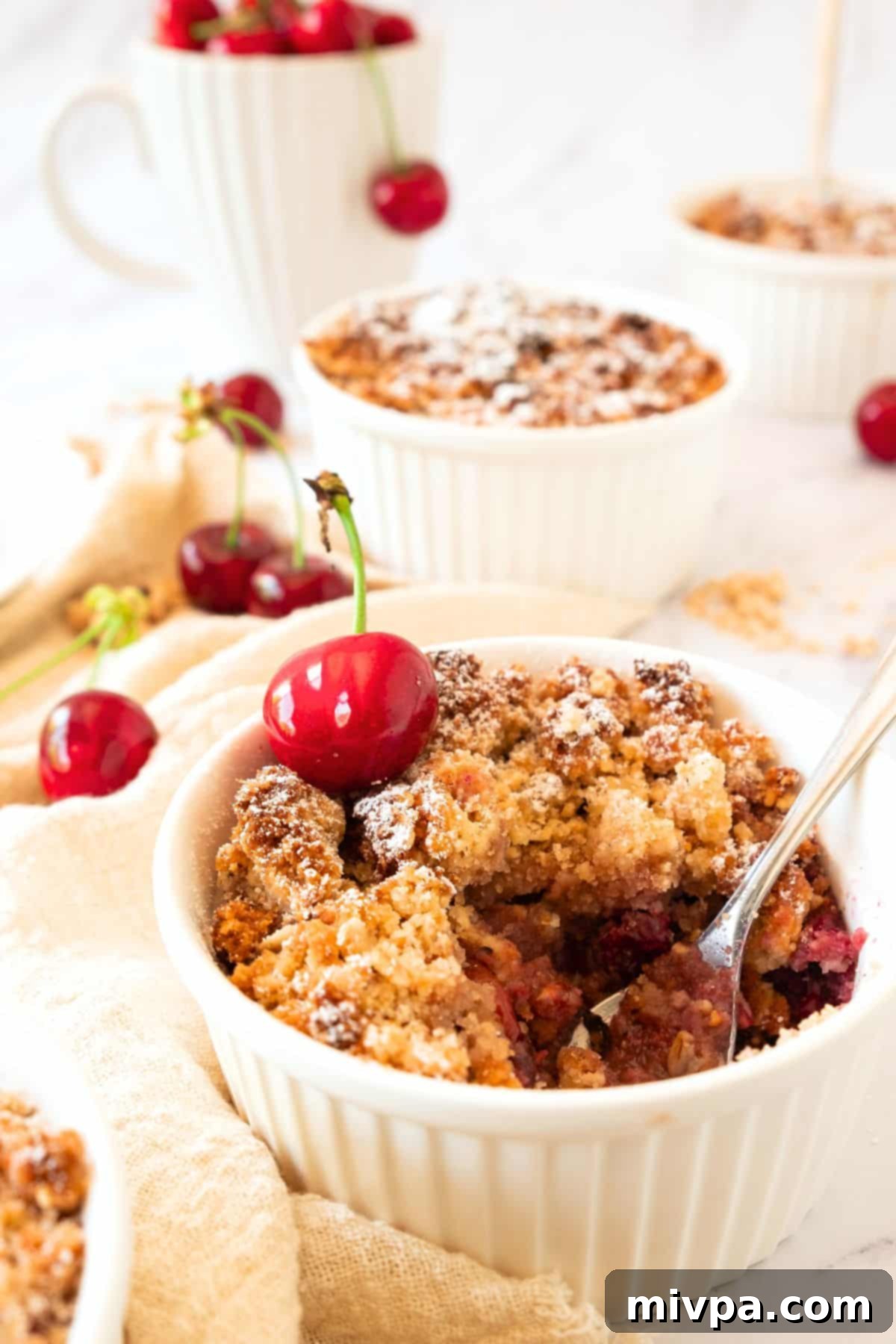 Cherry Crumble Recipe (Gluten-Free, Vegan) Up close shot of a half-eaten cherry crumble in a ramekin, revealing the juicy cherry filling and crispy topping.