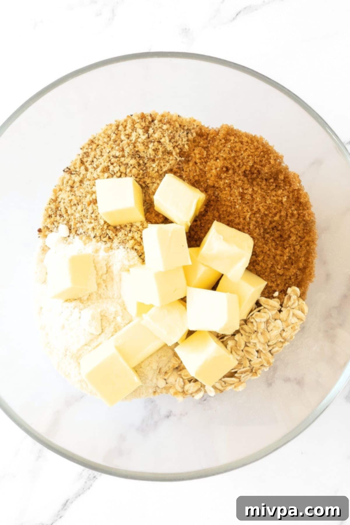 Gluten-Free Cherry Crumble Recipe A bowl containing the dry ingredients for the crumble topping: sugar, almond meal, gluten-free flour, rolled oats, and cold cubed butter, ready to be mixed.