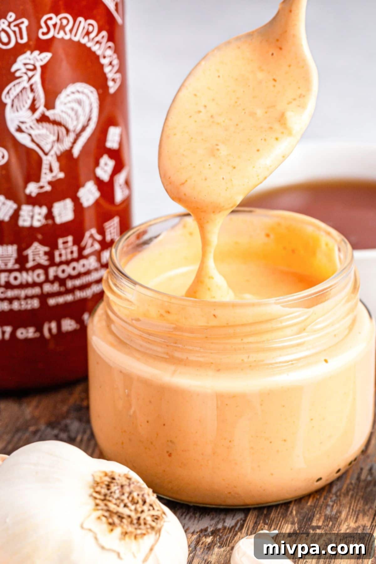 Holding up a spoonful of sriracha aioli from a jar.