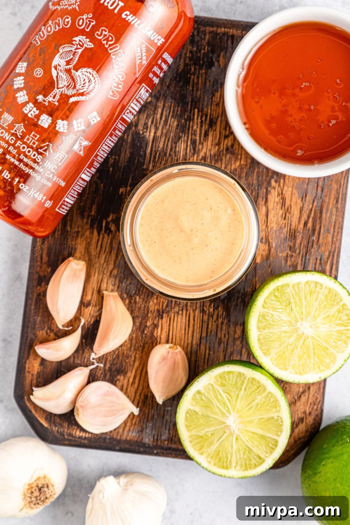 Garlic cloves, lime wedges, Sriracha and sriracha aioli on wooden board.