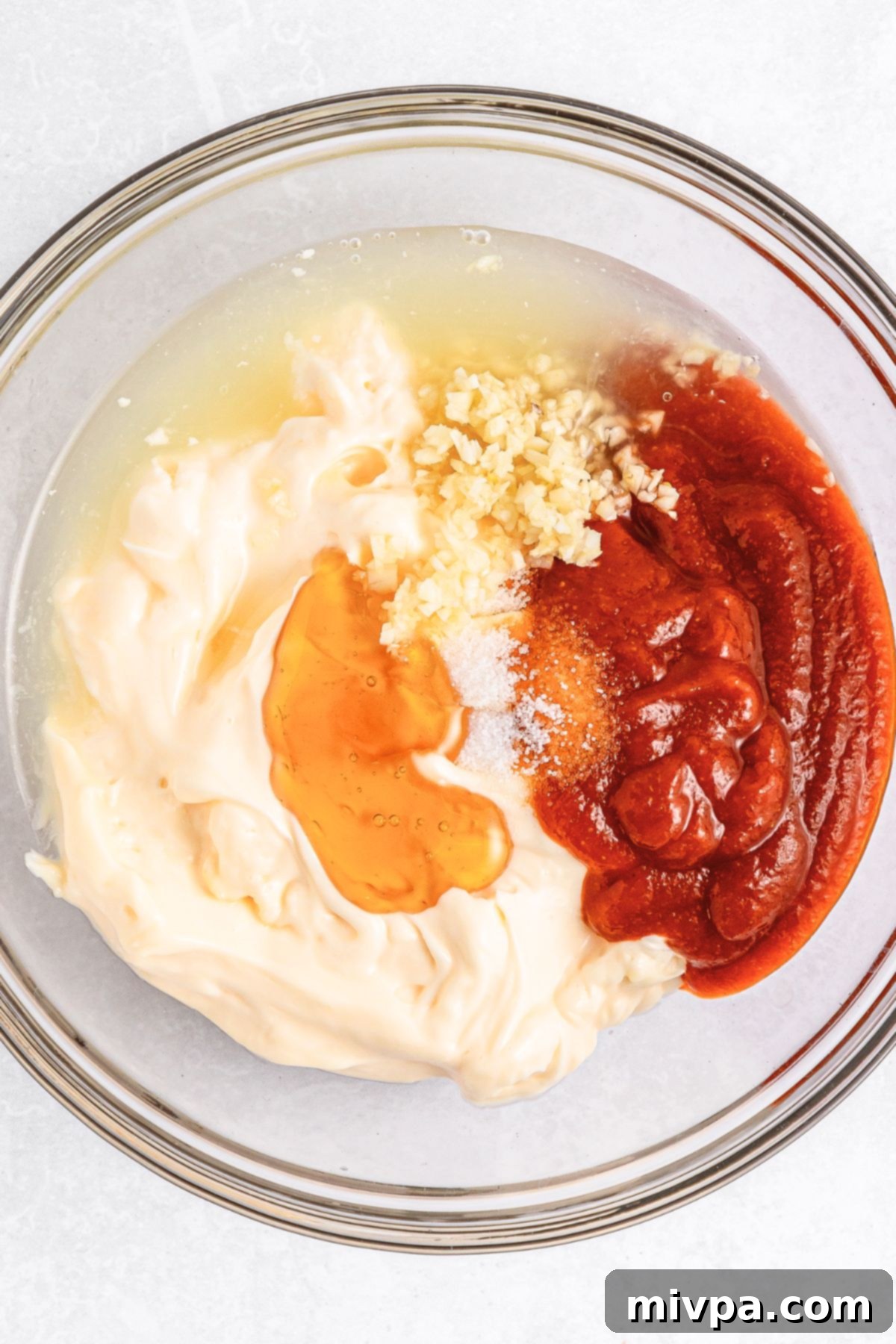 Sriracha sauce, mayonnaise, honey, minced garlic and lime juice in a glass bowl.