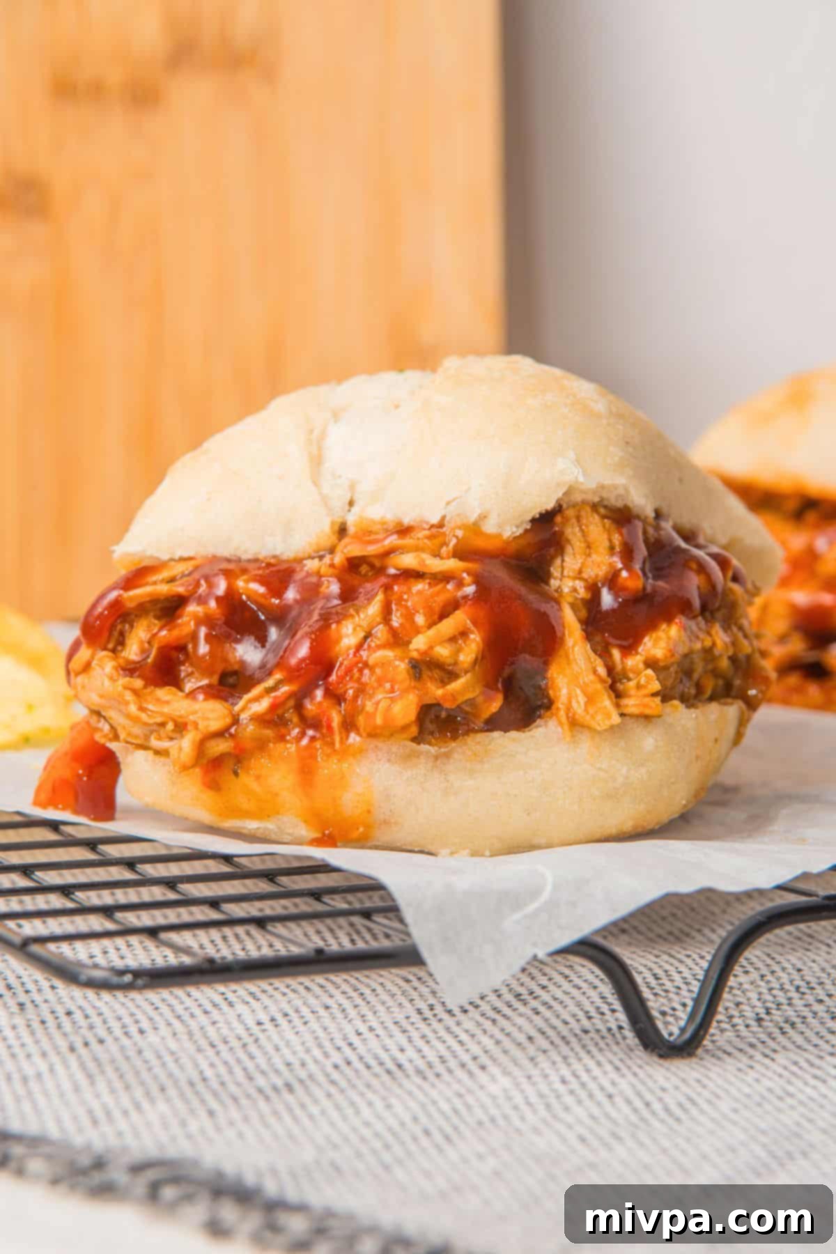 Up close image of a gluten-free pulled pork sandwich on parchment.