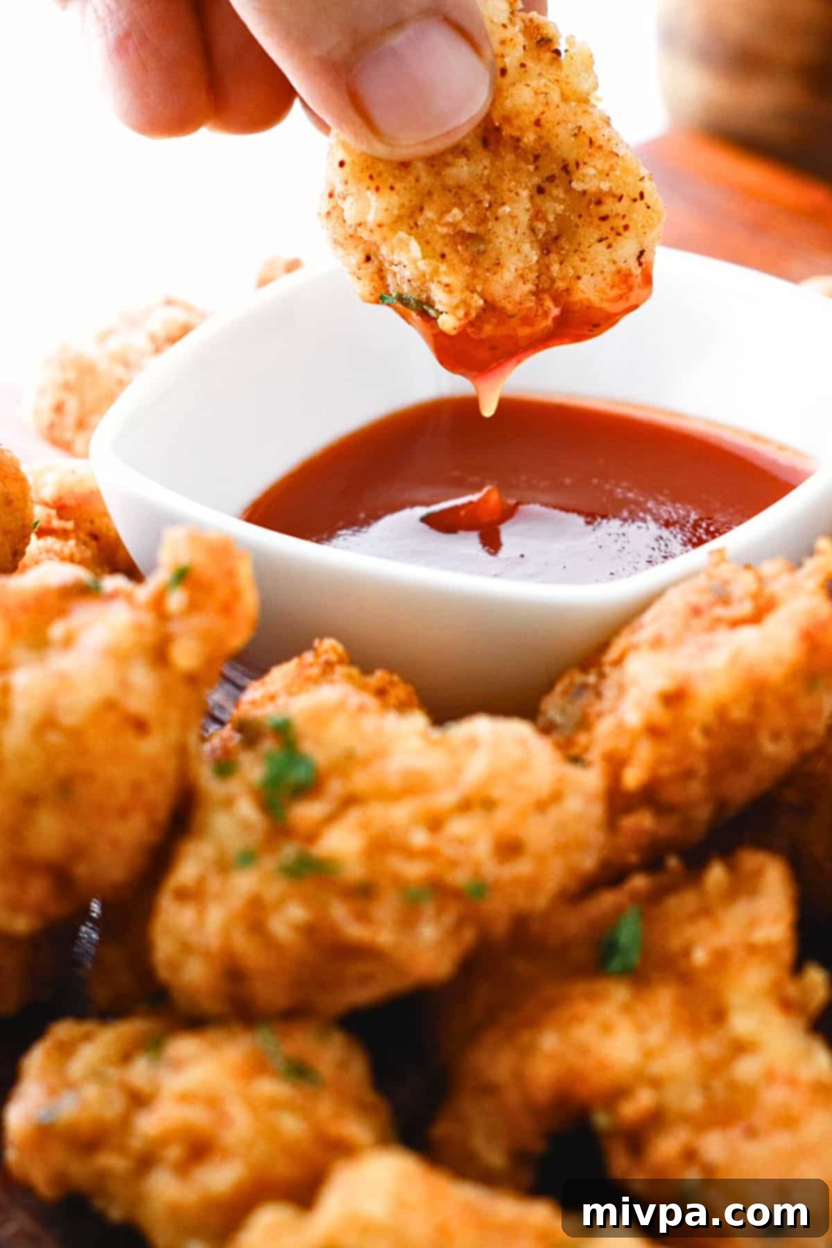 Dipping gluten-free popcorn chicken in a bowl of chili sauce.