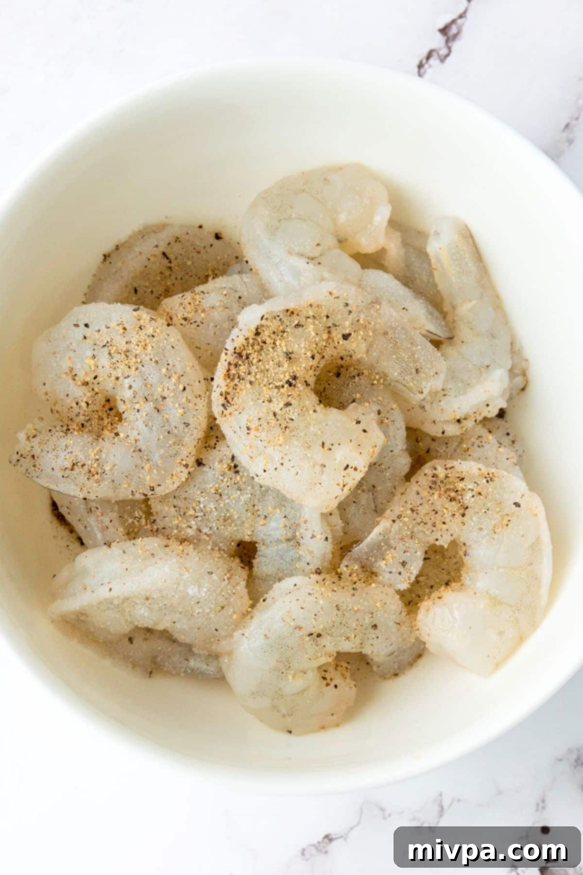 Gluten-Free Dairy-Free Bang Bang Shrimp Top down view of bowl of raw shrimp seasoned with salt and pepper.
