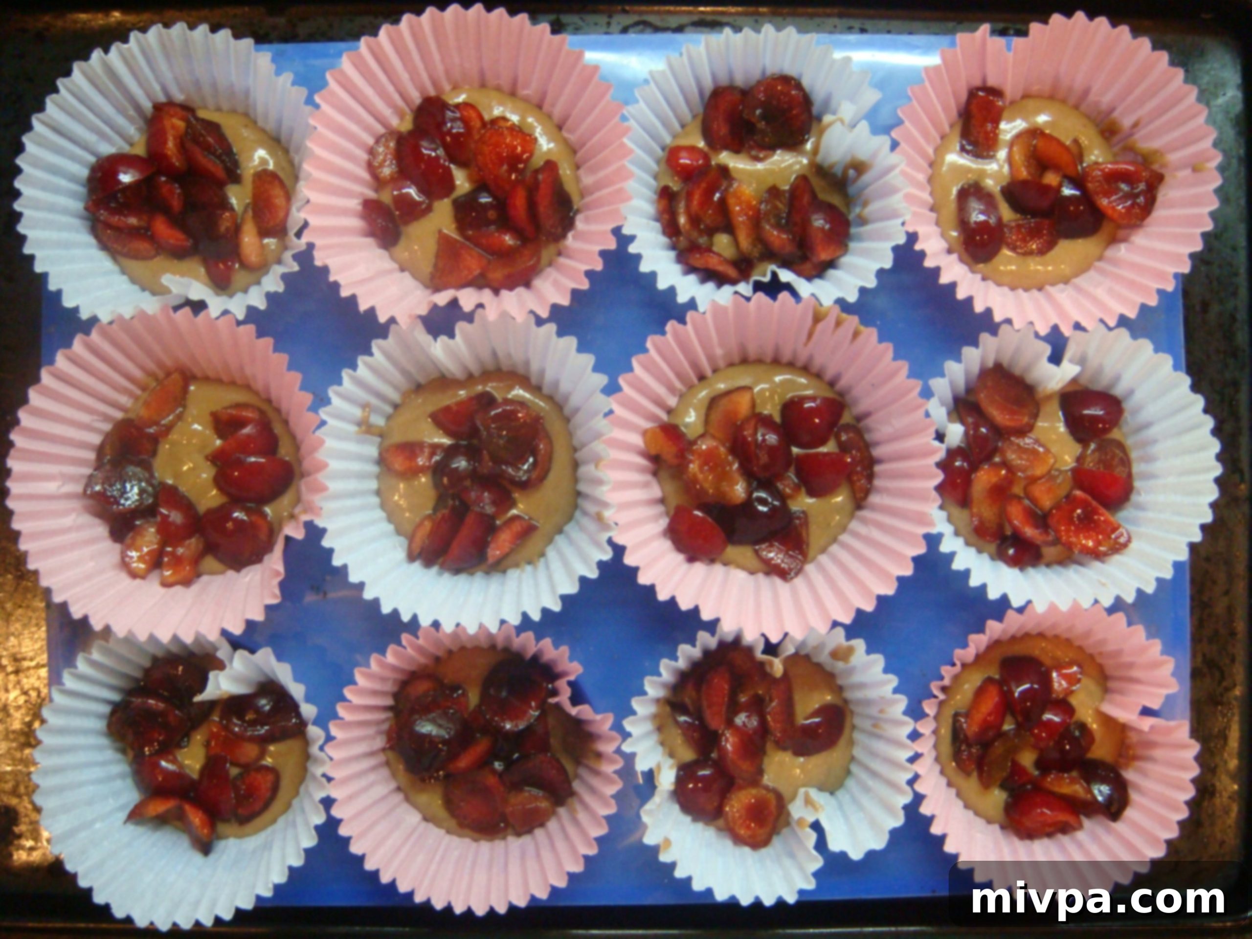 A teaspoon of chopped cherry pieces delicately placed on top of the initial layer of muffin batter in each cup.