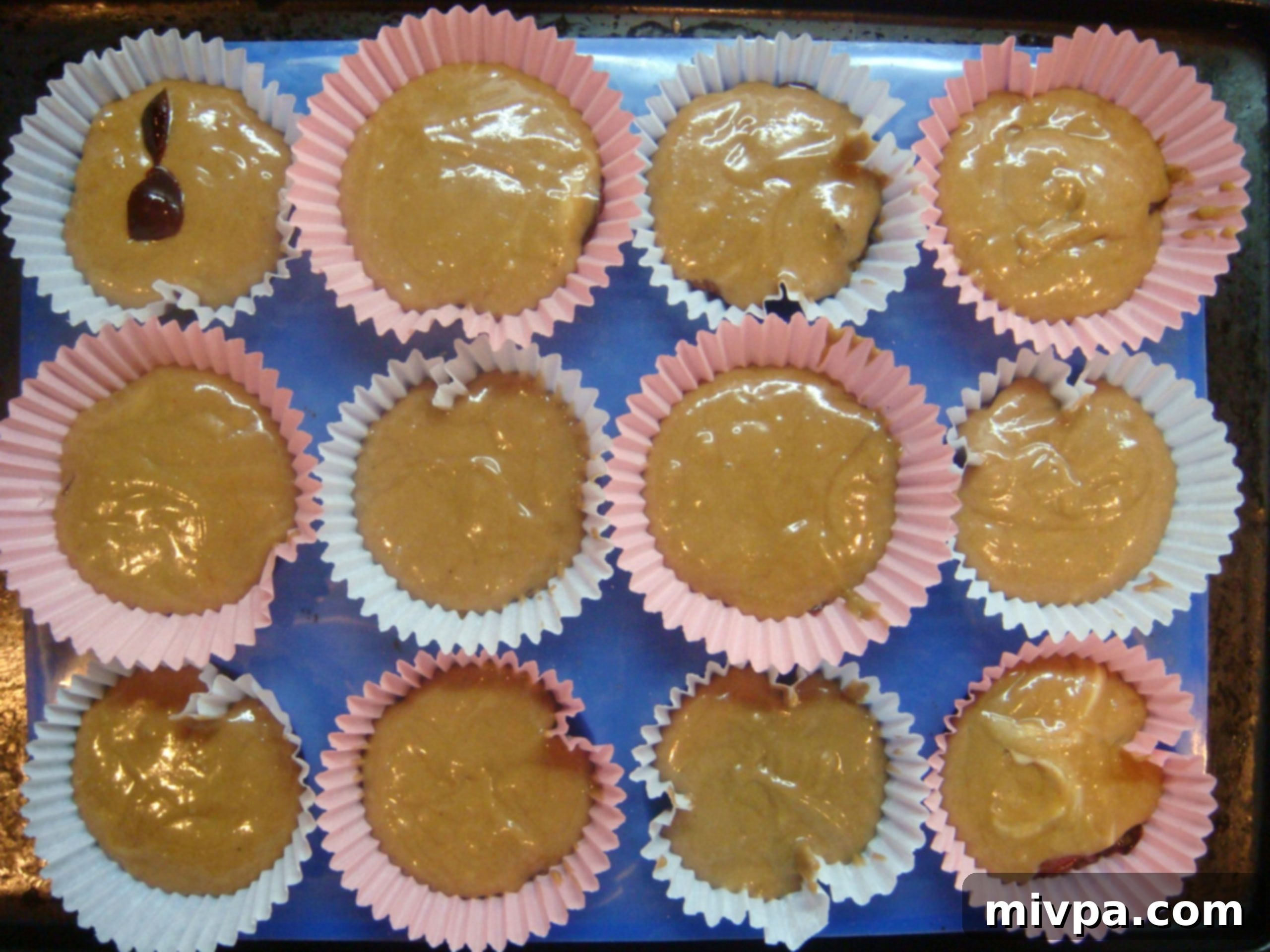 Muffin cups filled three-quarters full with batter after the cherry bits have been added, ready for baking.