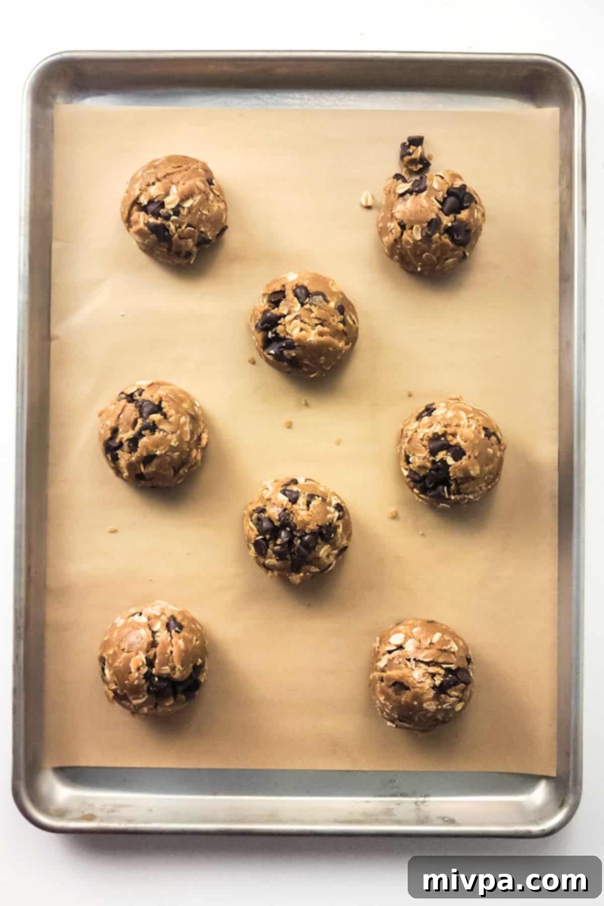 Scooping Dairy-Free Oatmeal Cookie Dough onto Baking Sheet Portioned balls of dairy-free oatmeal cookie dough neatly arranged on a parchment-lined cookie sheet, ready for baking.