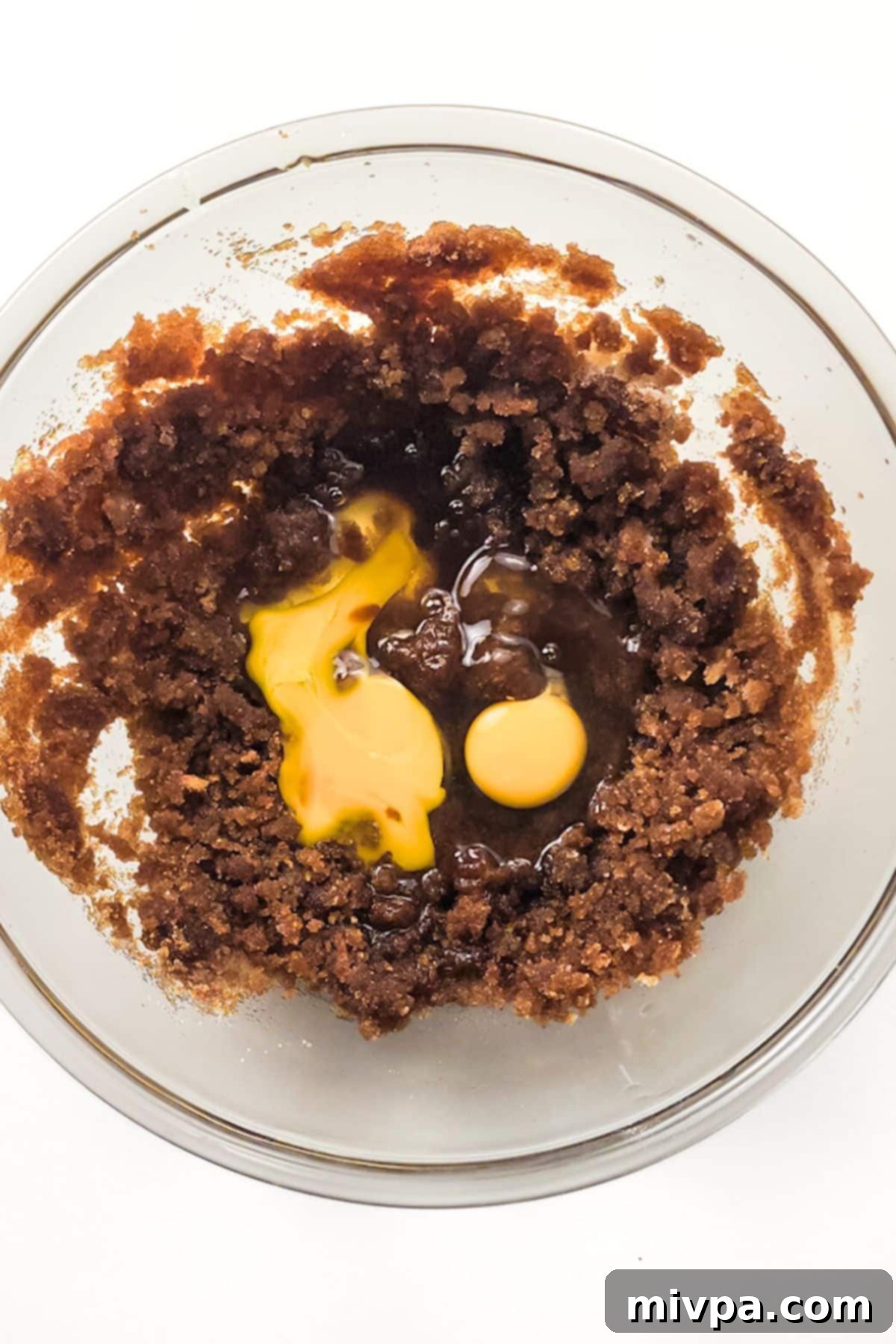 Blending Eggs and Vanilla into Cookie Dough Base Eggs and vanilla extract added to the butter and sugar mixture in a bowl, ready for blending.