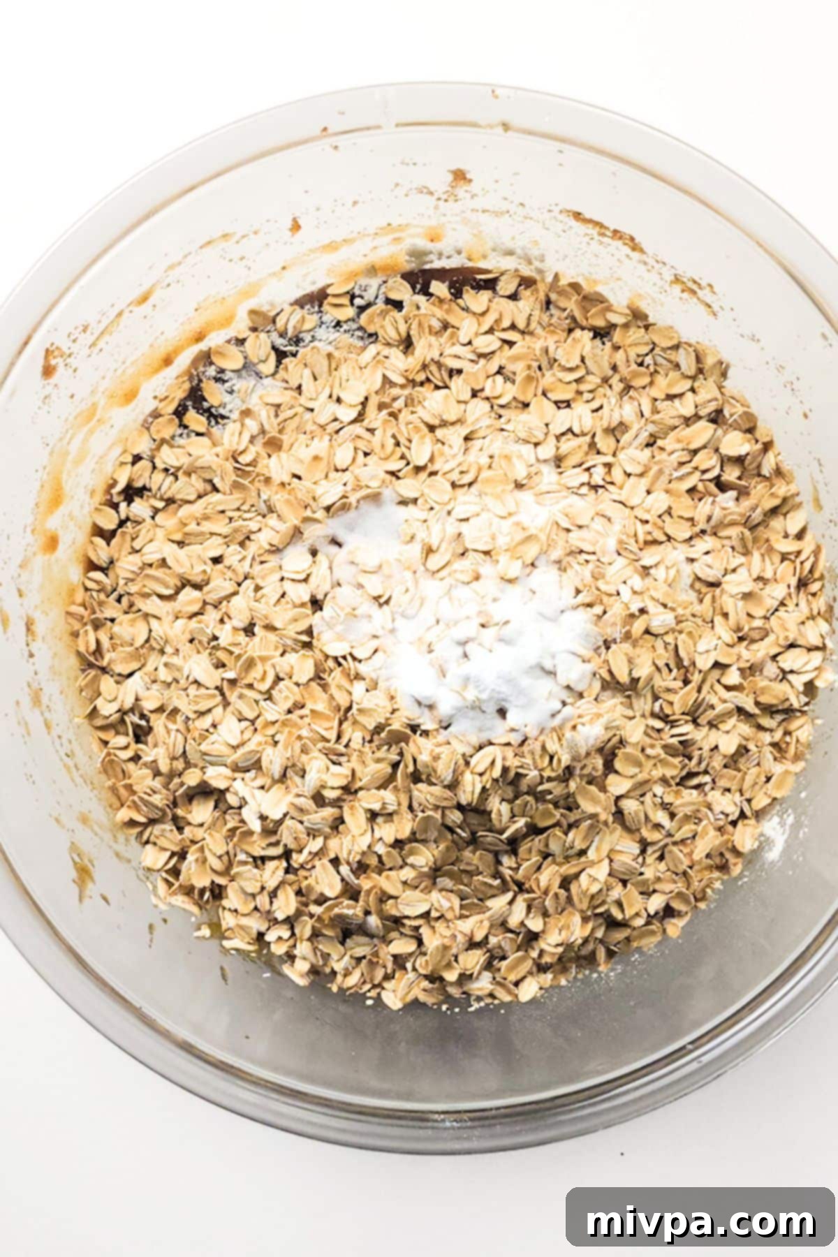 Mixing Dry Ingredients into Gluten-Free Oatmeal Cookie Dough A bowl of dry ingredients, including oats and gluten-free flour, placed on top of the wet butter mixture, ready to be combined.