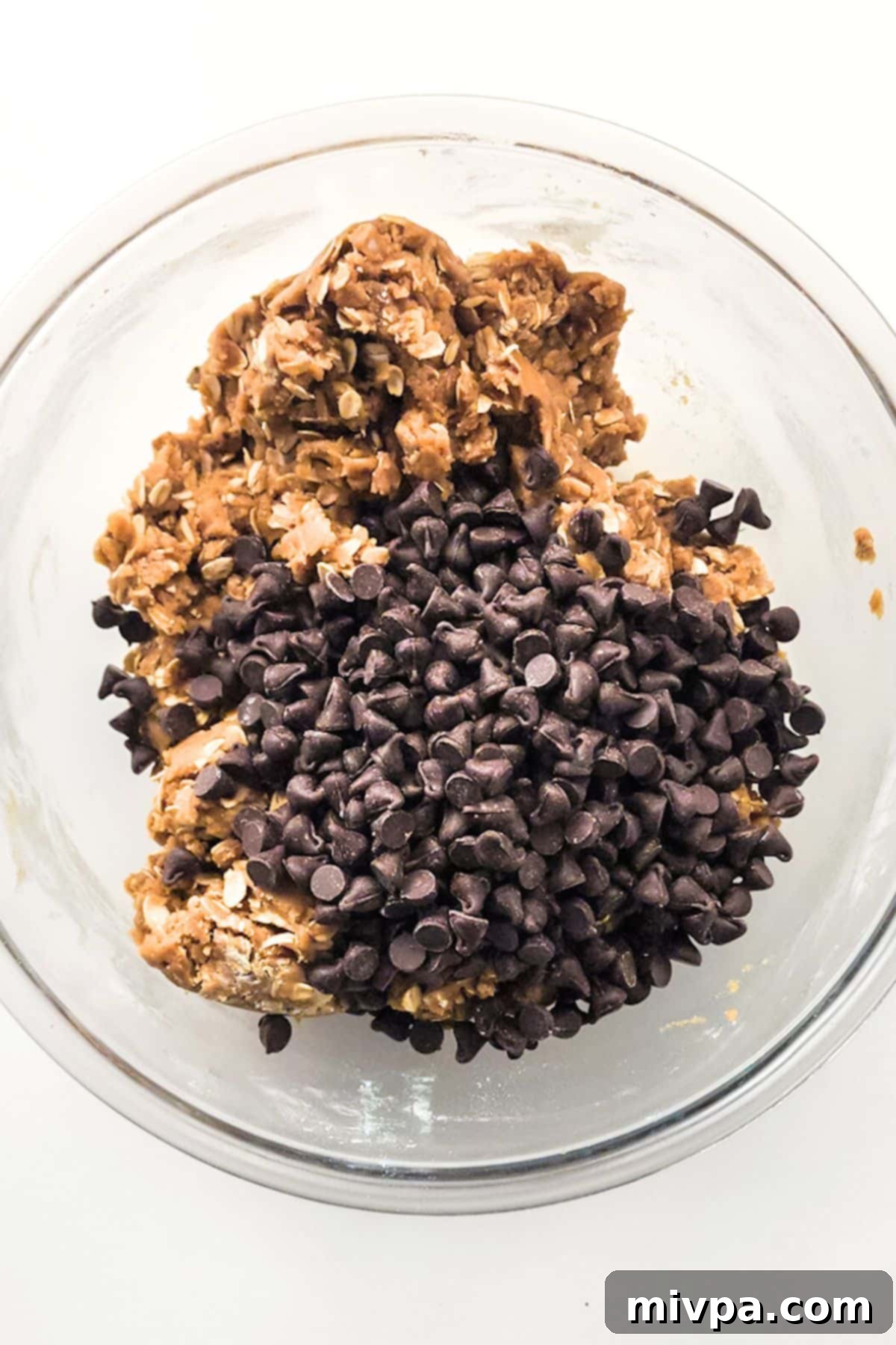 Folding Chocolate Chips into Oatmeal Cookie Dough Dairy-free chocolate chips folded into the gluten-free oatmeal cookie dough in a mixing bowl.