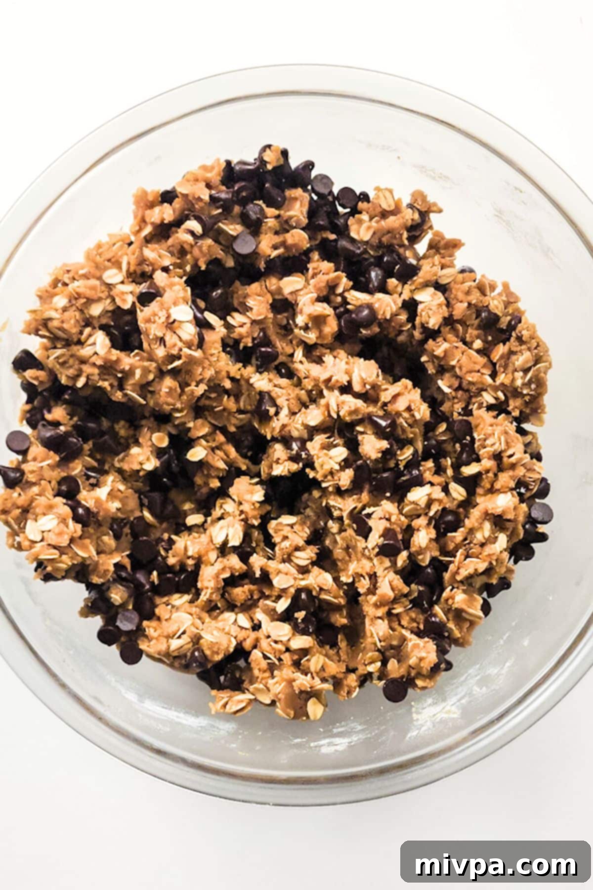 Gluten-Free Chocolate Chip Oatmeal Cookie Dough Resting A bowl of chocolate chip oatmeal cookie dough covered with plastic wrap, resting at room temperature.