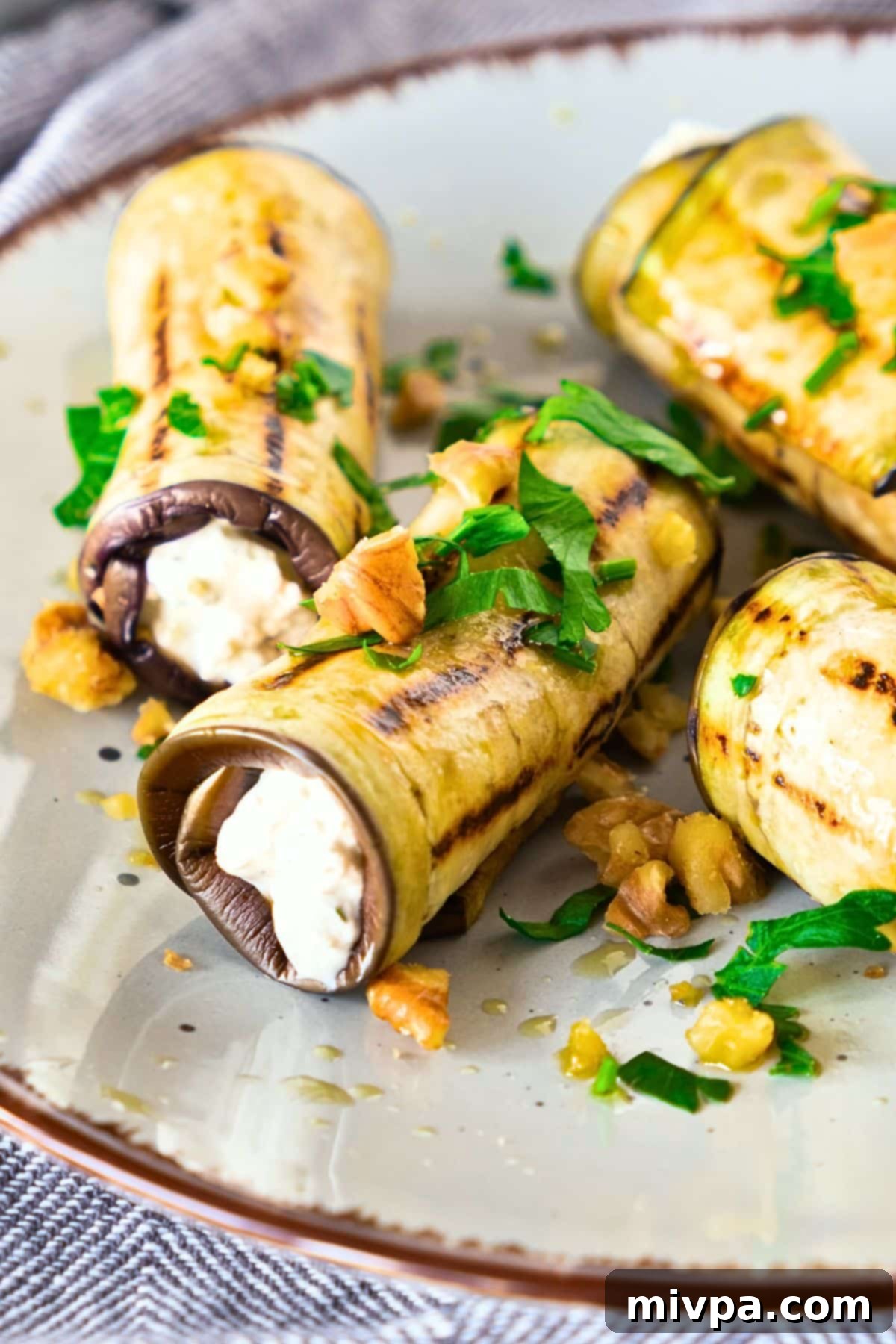 A beautifully arranged plate of eggplant roll ups, garnished with fresh chopped parsley and a light drizzle of olive oil, ready to be served as a savory appetizer.