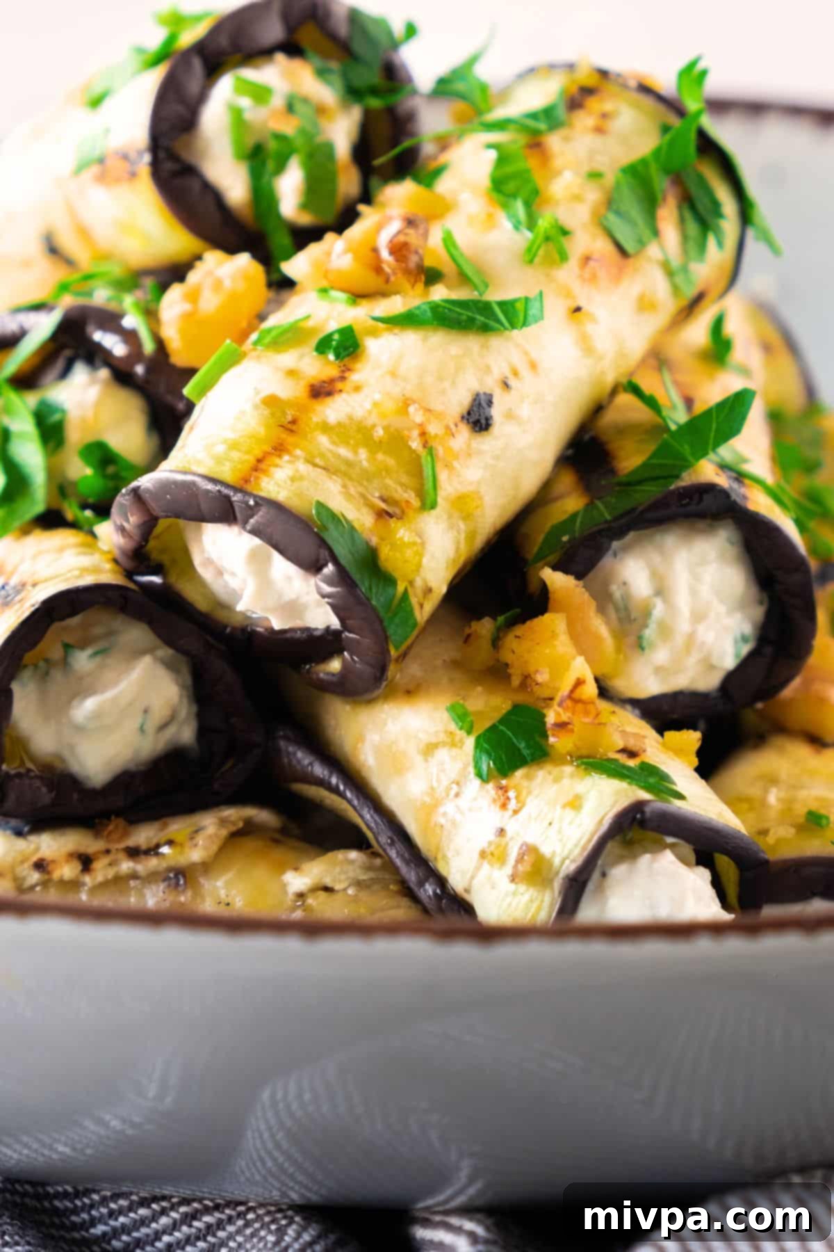 Close-up shot of a bowl filled with freshly prepared eggplant roll ups, showcasing their appealing texture and appetizing appearance.