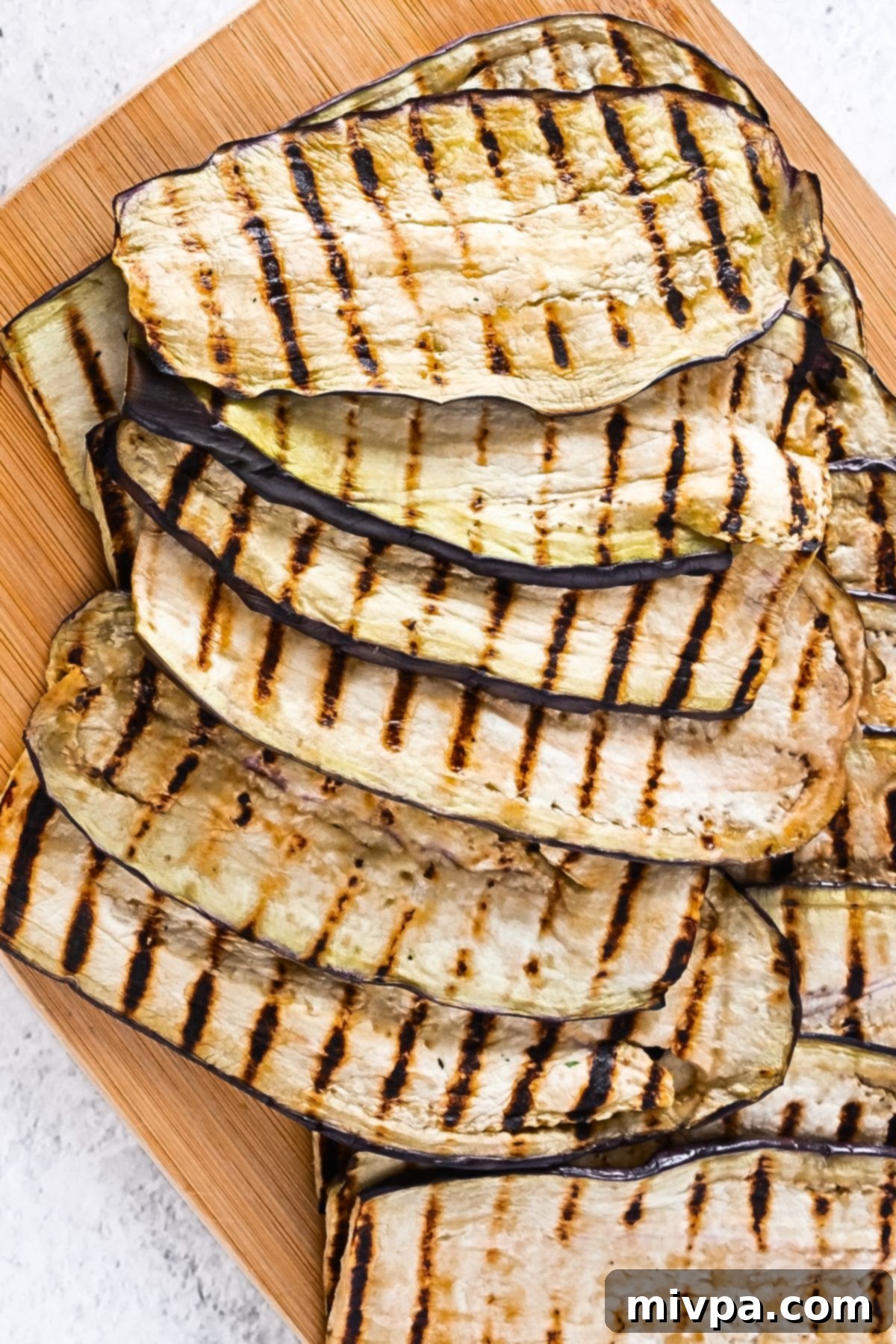 Close-up of perfectly grilled eggplant slices, displaying appealing char marks and a tender texture, cooling on a plate.