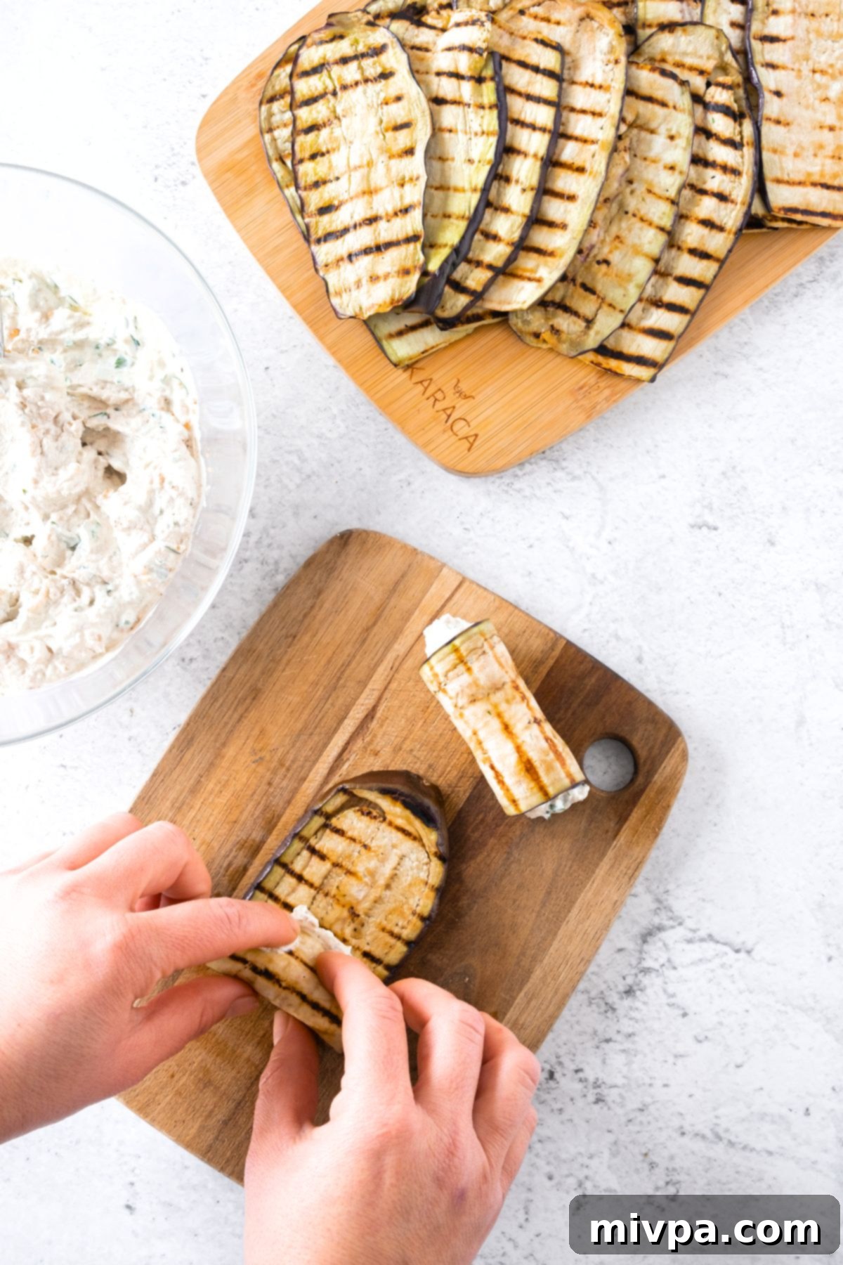 A close-up shot of the assembly process, showing an eggplant slice being rolled around a dollop of creamy filling on a wooden board.