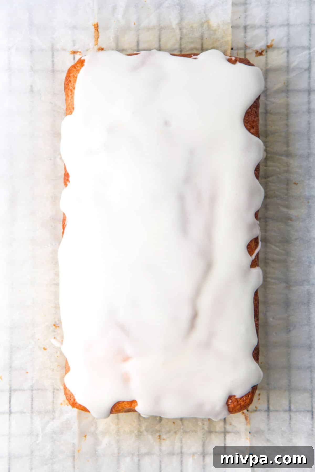 Gluten-Free Lemon Drizzle Cake (Dairy-Free) Lemon Drizzle Cake with glaze being poured over it, on parchment paper.