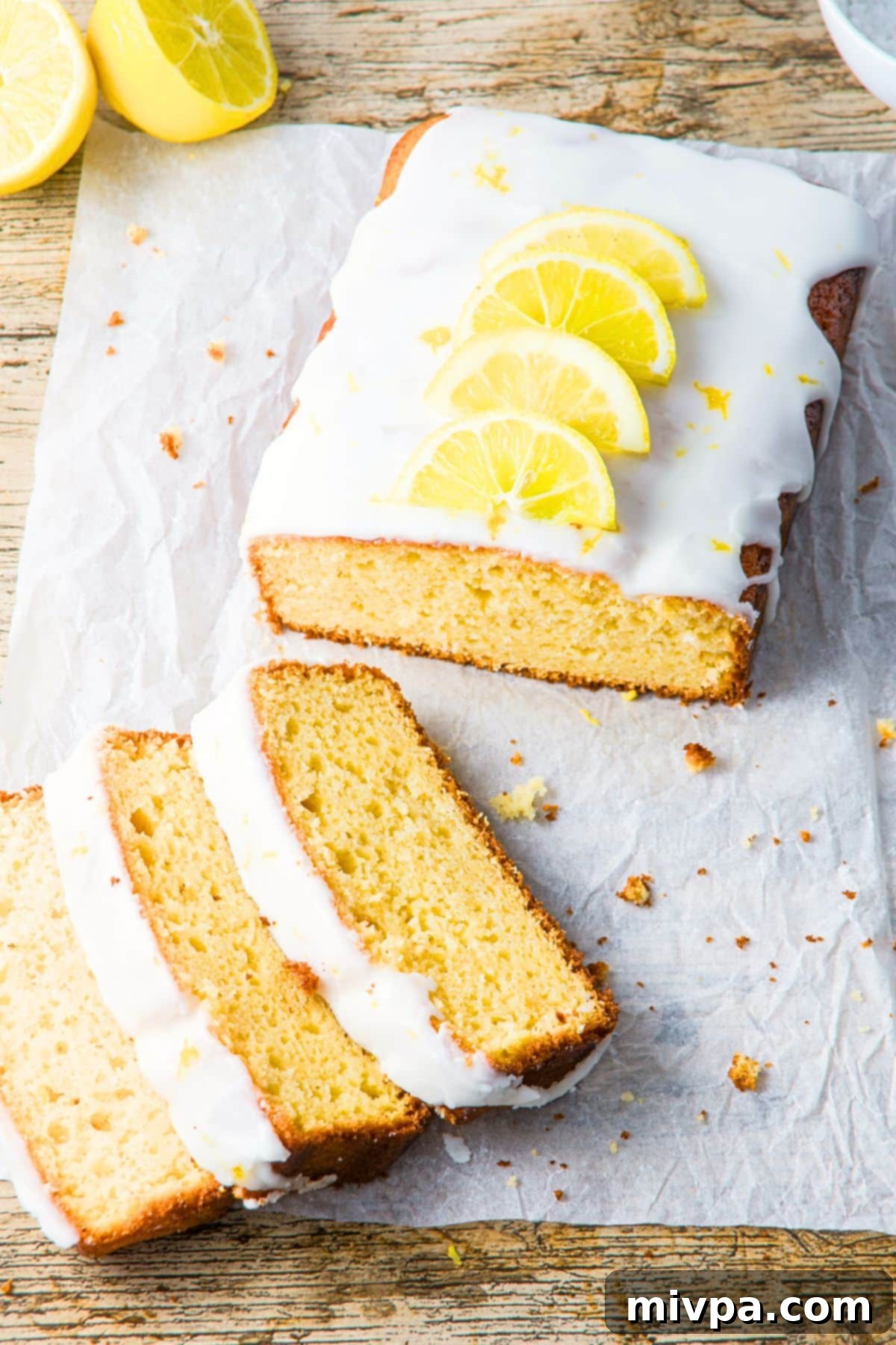 Lemon Drizzle Cake (Gluten-Free, Dairy-Free) A half-sliced loaf of gluten-free lemon drizzle cake on parchment paper, ready to be served.
