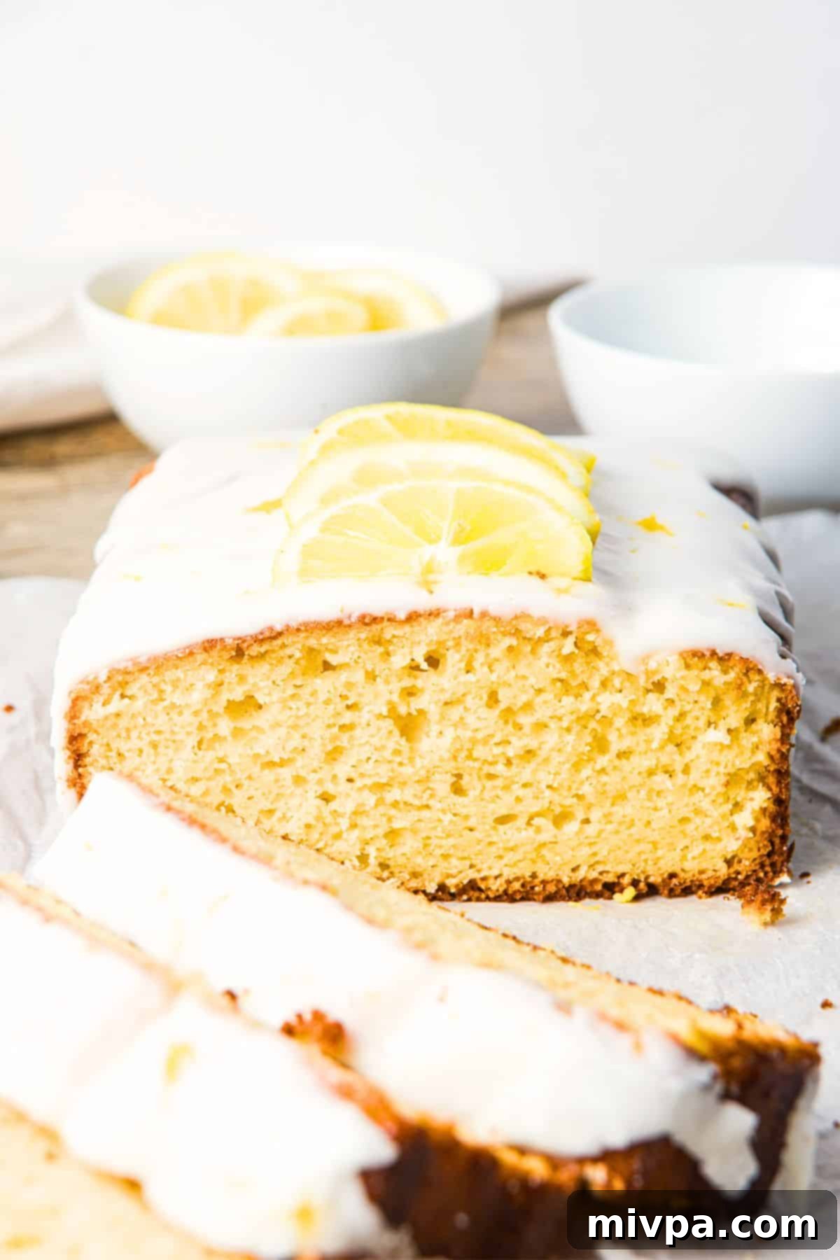 Lemon Drizzle Cake Half-eaten lemon drizzle cake topped with sliced lemons and zest, showcasing its moist texture.