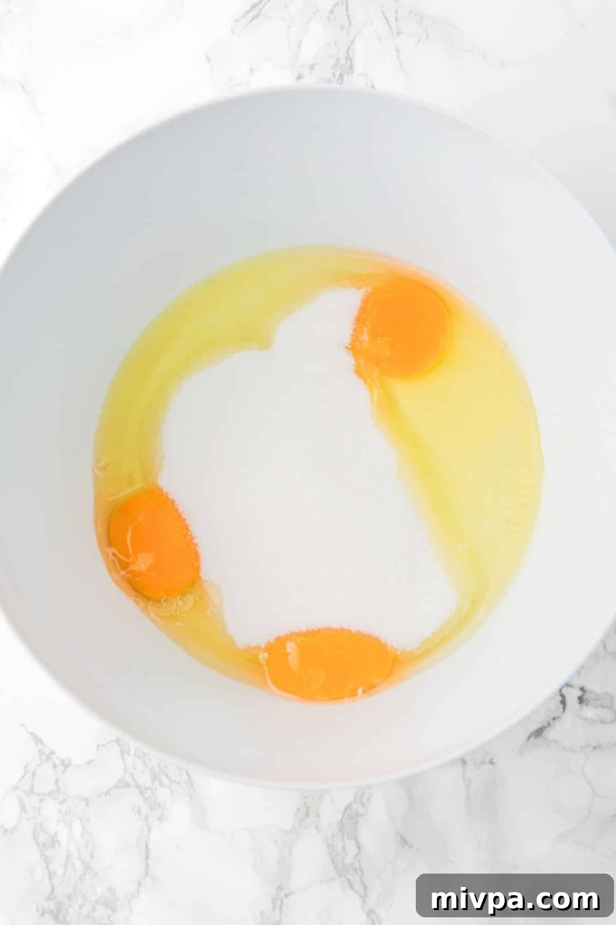 Gluten-Free Lemon Drizzle Loaf Cake Batter Prep Close-up of eggs and sugar being beaten together in a large mixing bowl.