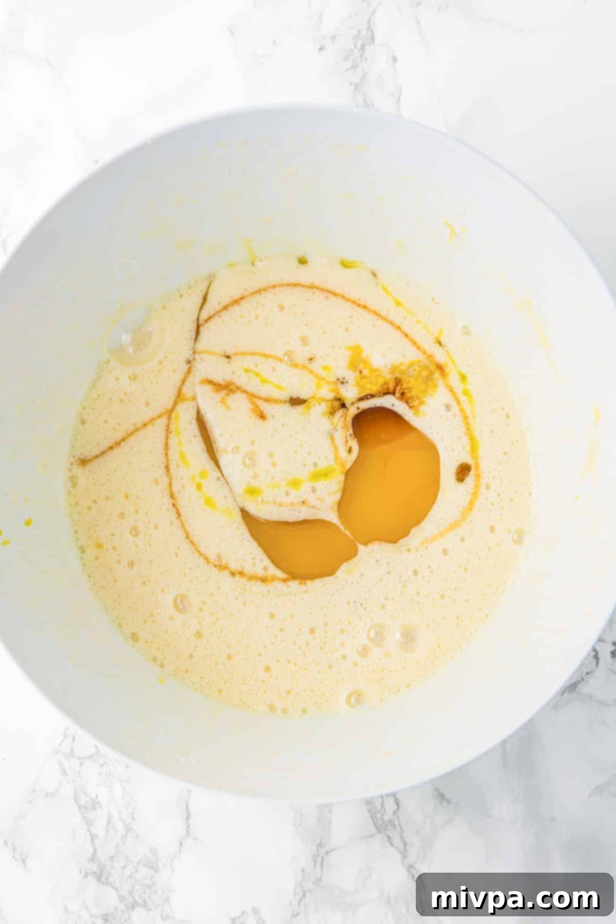 Gluten Dairy-Free Lemon Drizzle Cake Egg, sugar, vanilla extract, lemon zest, and olive oil mixture in a bowl.