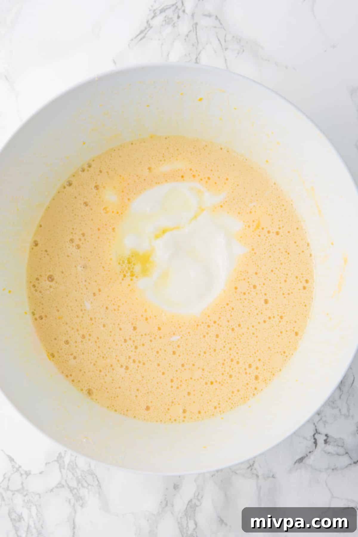 Lemon Drizzle Gluten-Free Cake Pale yellow wet batter mixture with dairy-free yogurt in a white bowl.