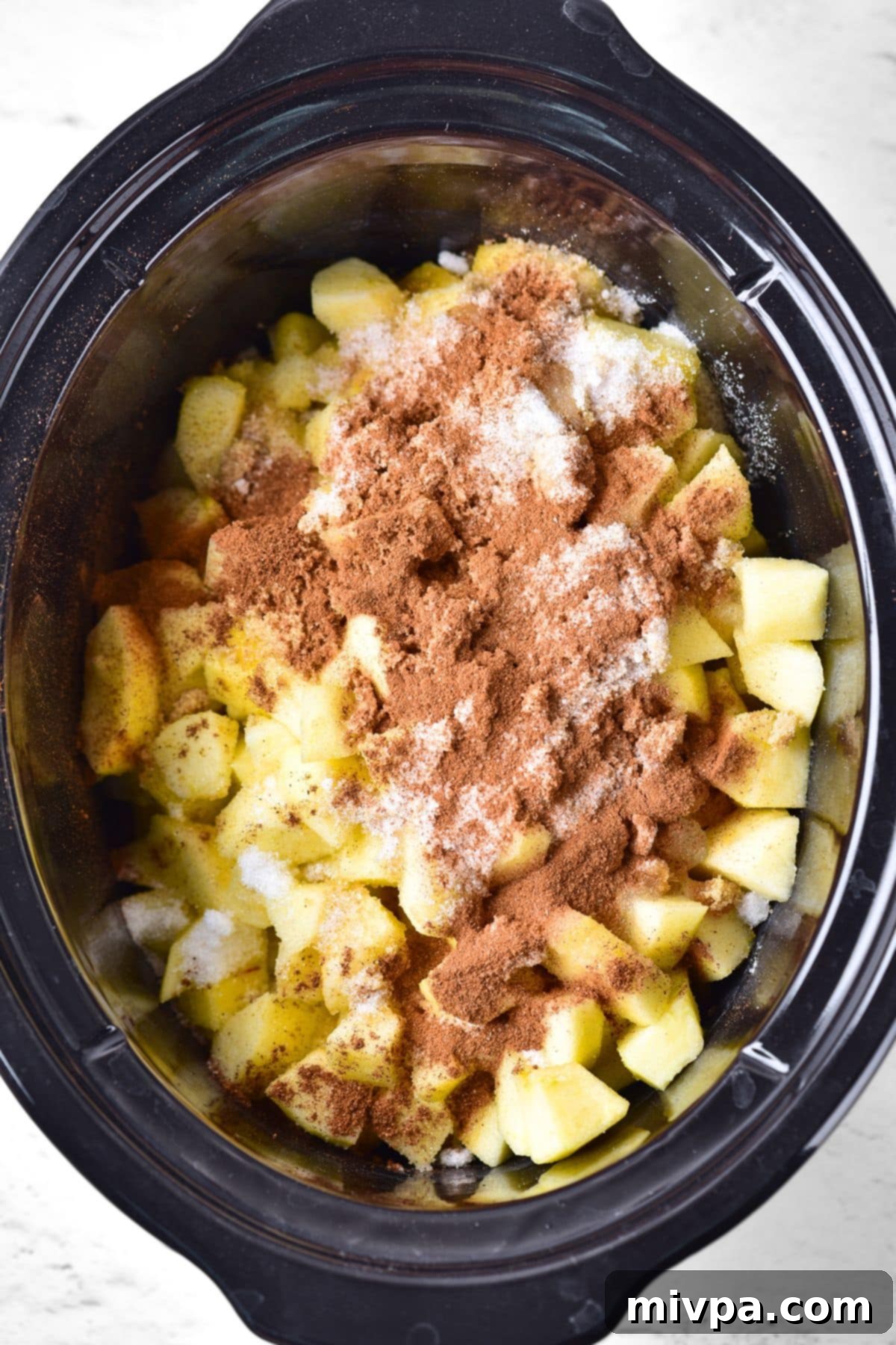 Cubed apples topped with spices in slow cooker bowl.