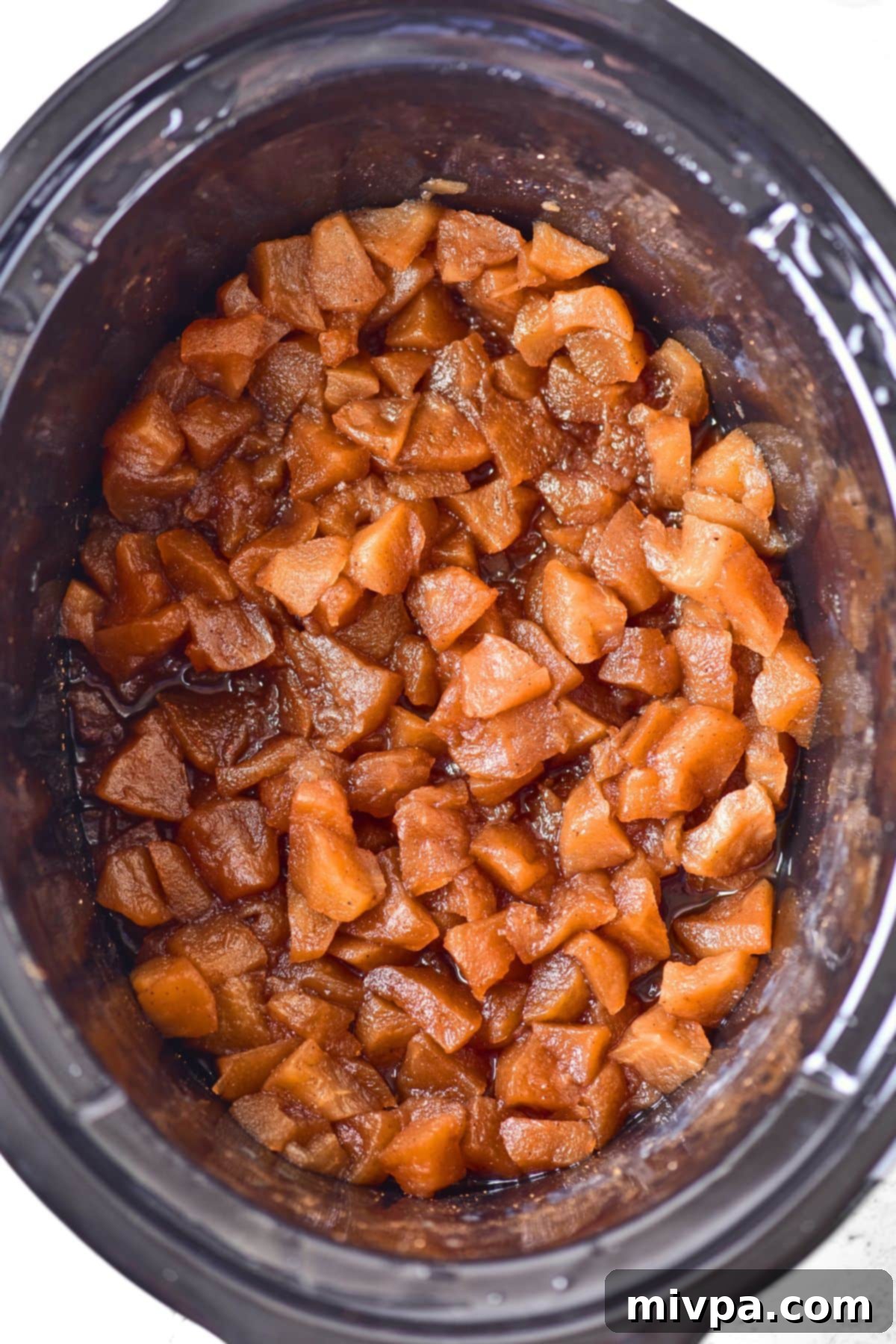 How to Make Apple Butter Close-up view of slow-cooked apple cubes, soft and slightly broken down, in the crockpot after several hours of cooking.