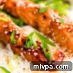 Teriyaki salmon fillets on rice, garnished with green onions and sesame seeds.