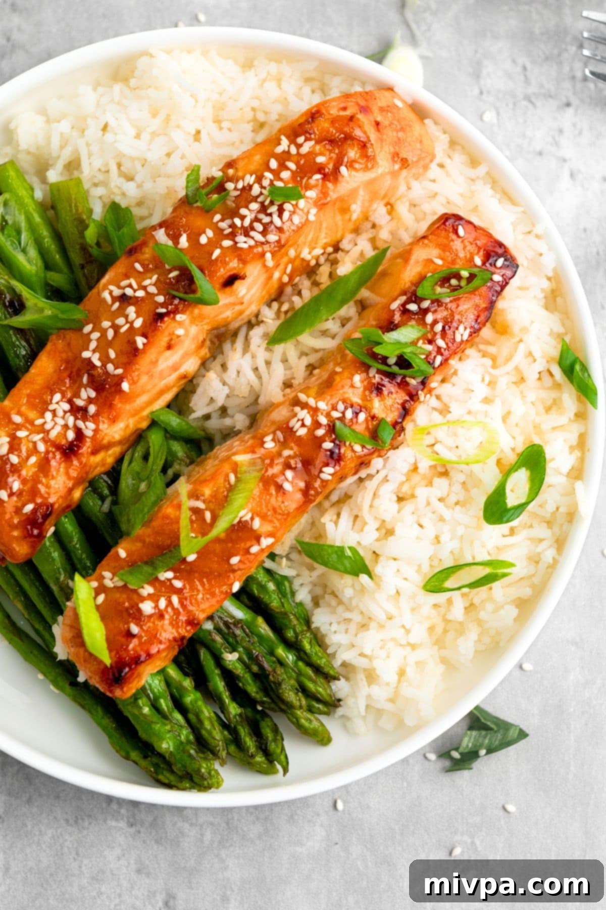 Top down view of two beautifully plated gluten-free teriyaki salmon bowls, garnished with sesame seeds and green onions, served with rice and vibrant vegetables.
