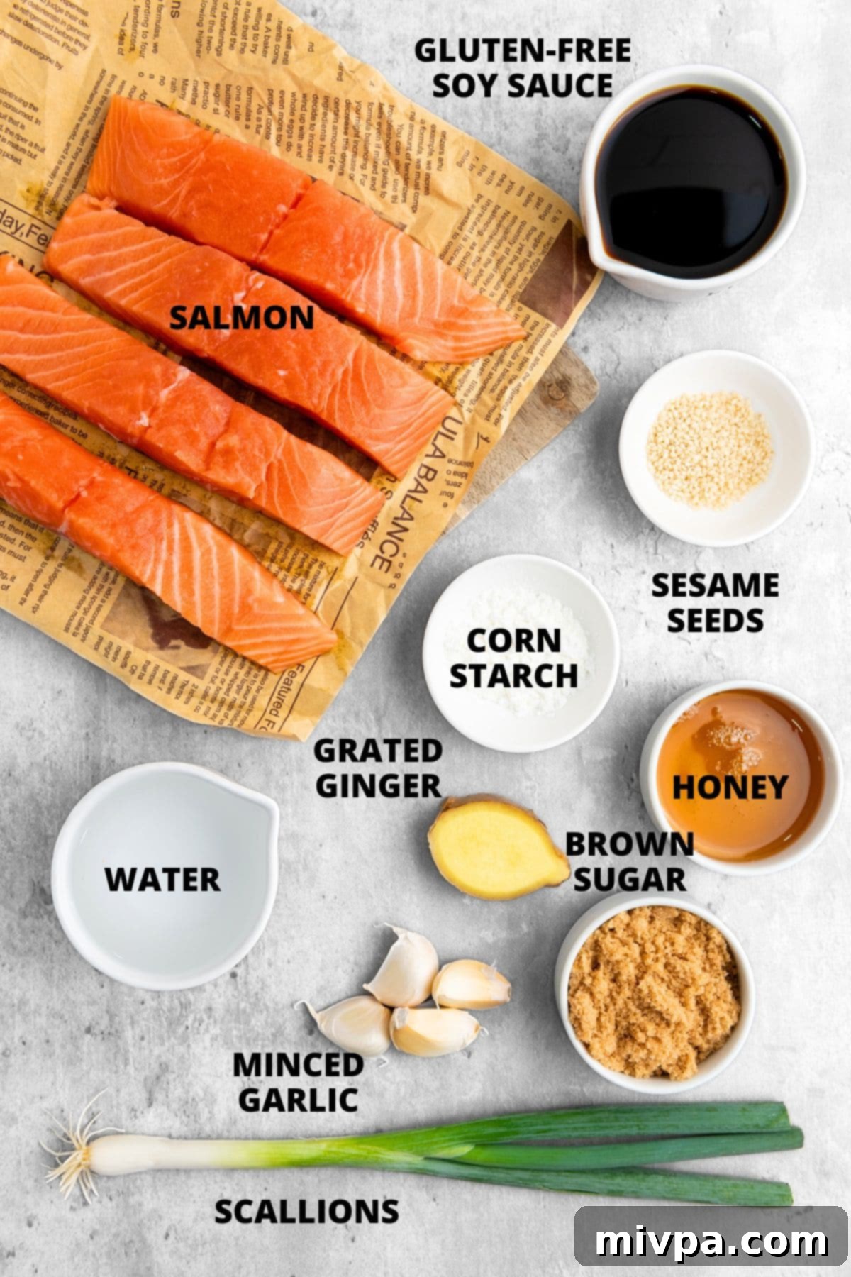A beautifully arranged selection of ingredients for a healthy teriyaki salmon bowl recipe, laid out on a clean grey board, including fresh salmon fillets, soy sauce, ginger, garlic, honey, brown sugar, cornstarch, scallions, and sesame seeds.