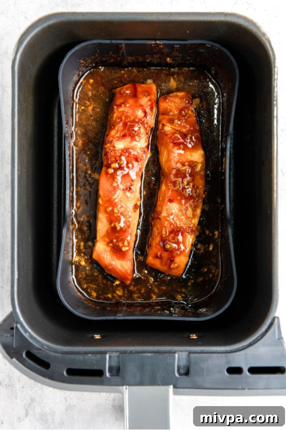 Teriyaki salmon cooking in an air fryer basket, showing the glaze beginning to caramelize on the fish.