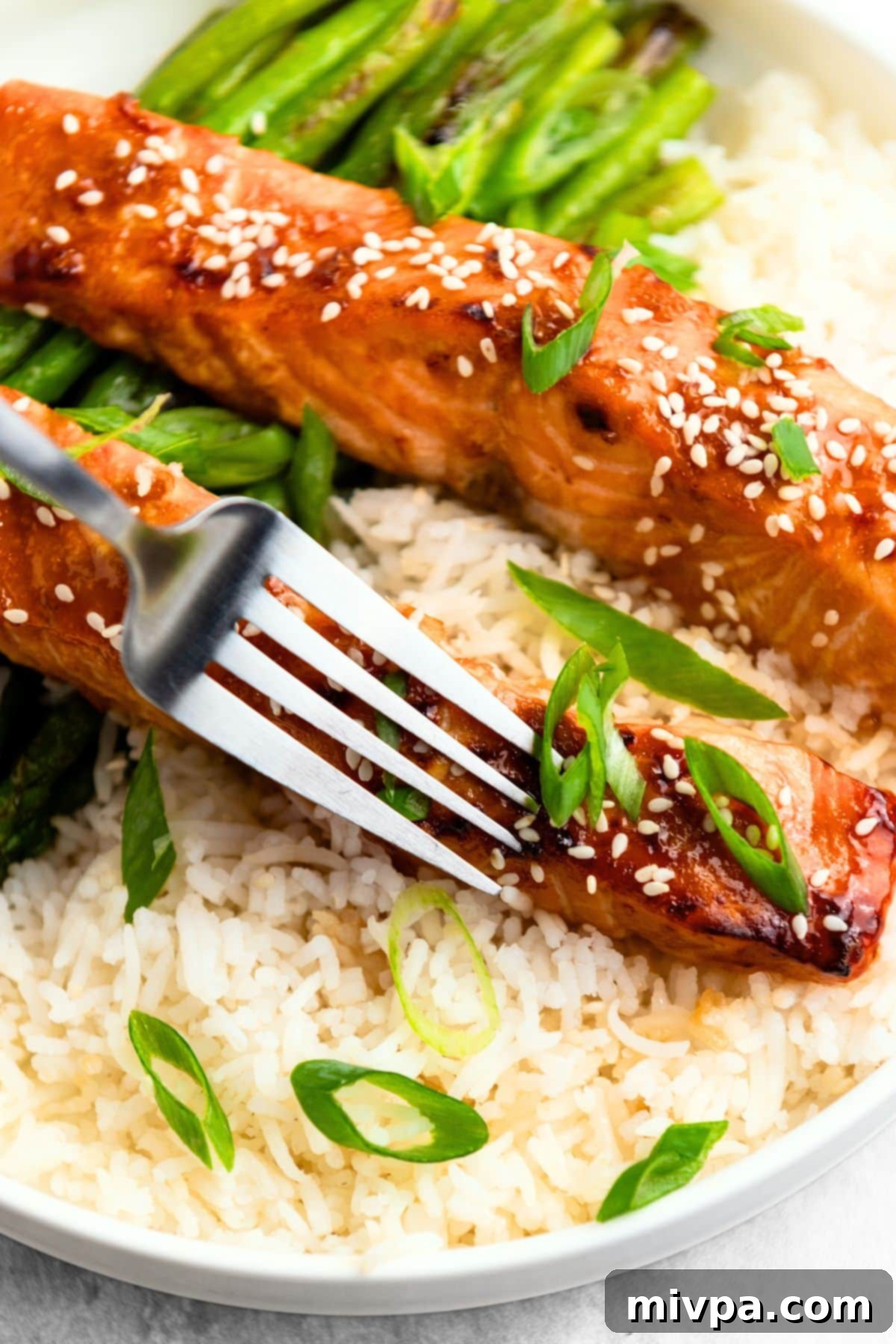 A fork piercing into a piece of perfectly cooked teriyaki salmon, showing its flaky texture and the delicious glaze.