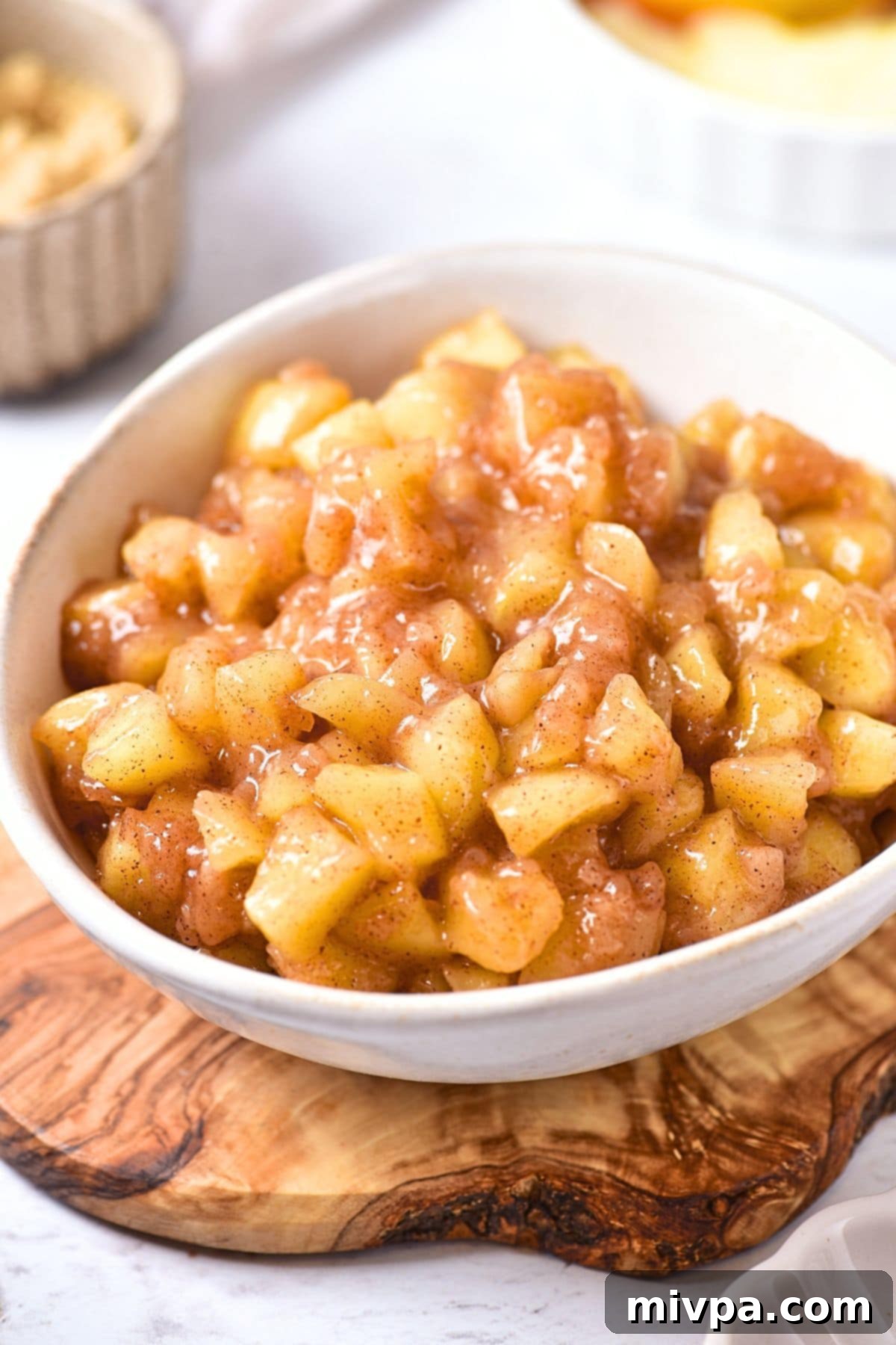 A bowl of rich, spiced gluten-free apple pie filling with perfectly cooked apple chunks, ready to be used in desserts or enjoyed on its own. Served on a rustic wooden board.