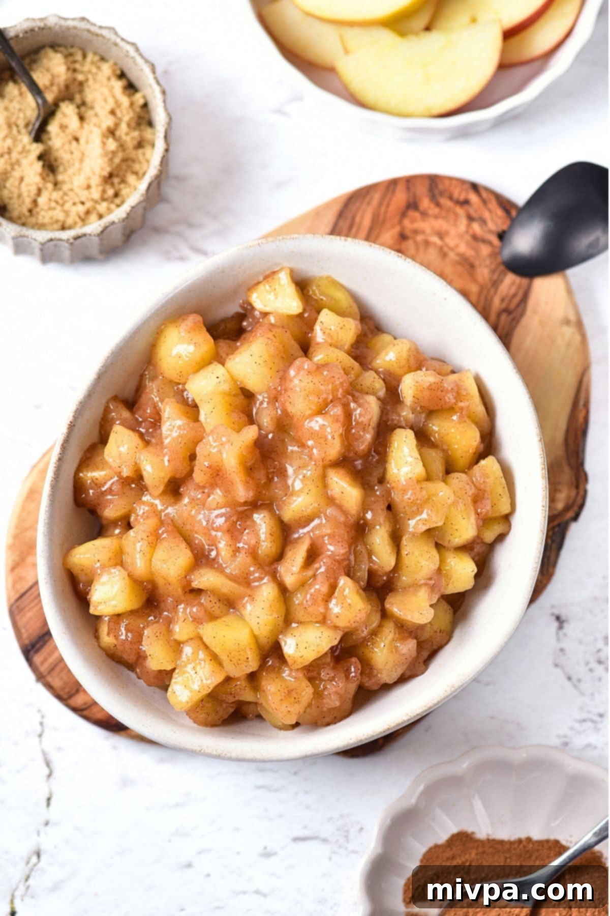 Top down view of a bowl of delicious homemade apple pie filling, showcasing the tender apple chunks and thick, glossy sauce, set on a rustic wooden board.