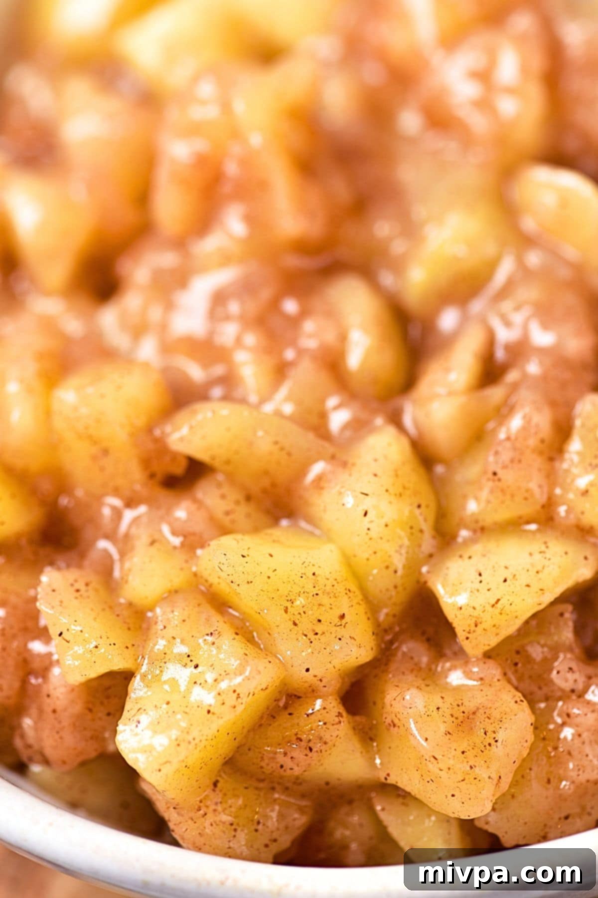 Up close view of a bowl of vibrant, glossy gluten-free dairy-free apple pie filling, showing the soft, tender apple pieces.