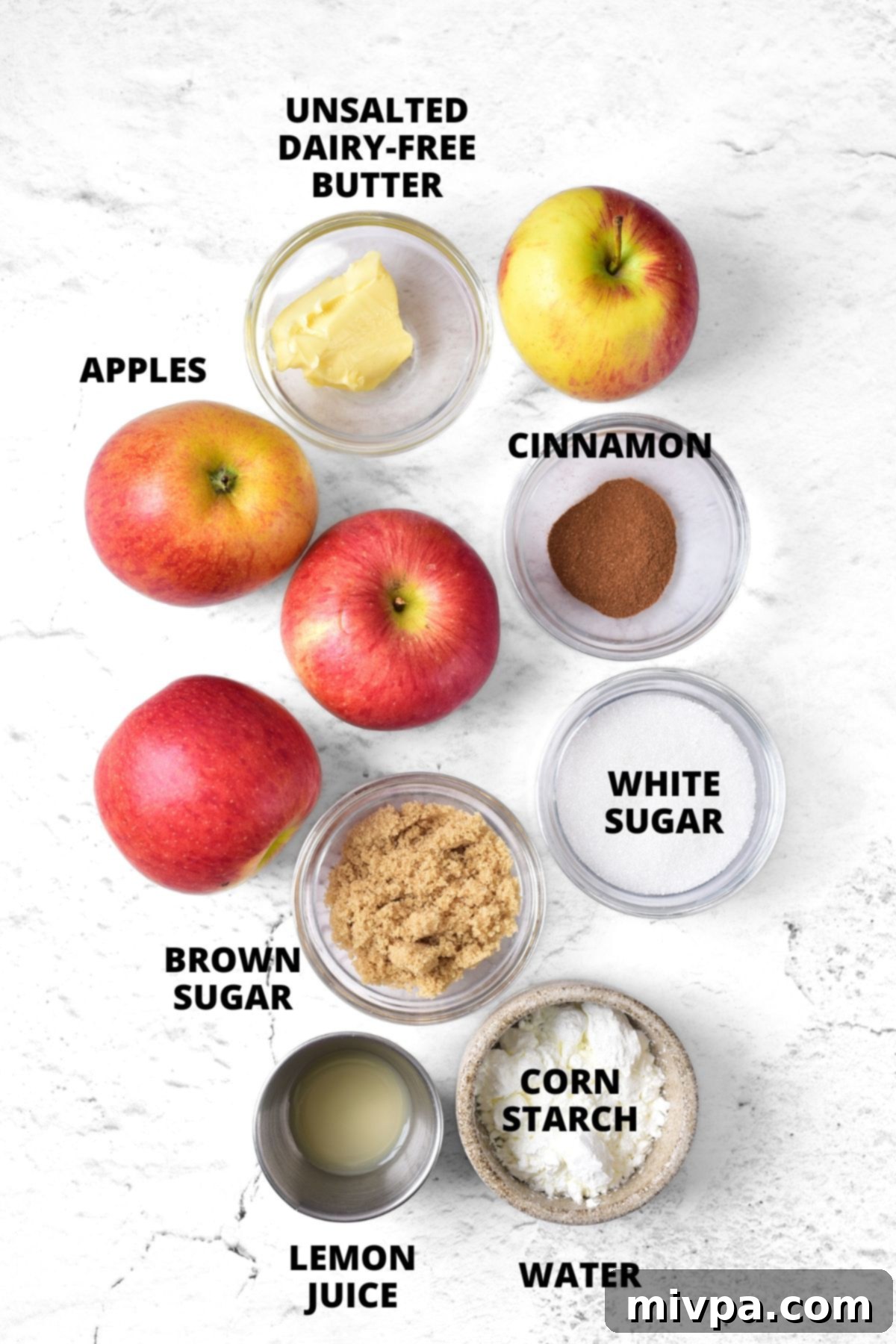 All the fresh ingredients for this gluten-free apple pie filling recipe, neatly laid out on a wooden board, including apples, sugars, cinnamon, lemon, and dairy-free butter.