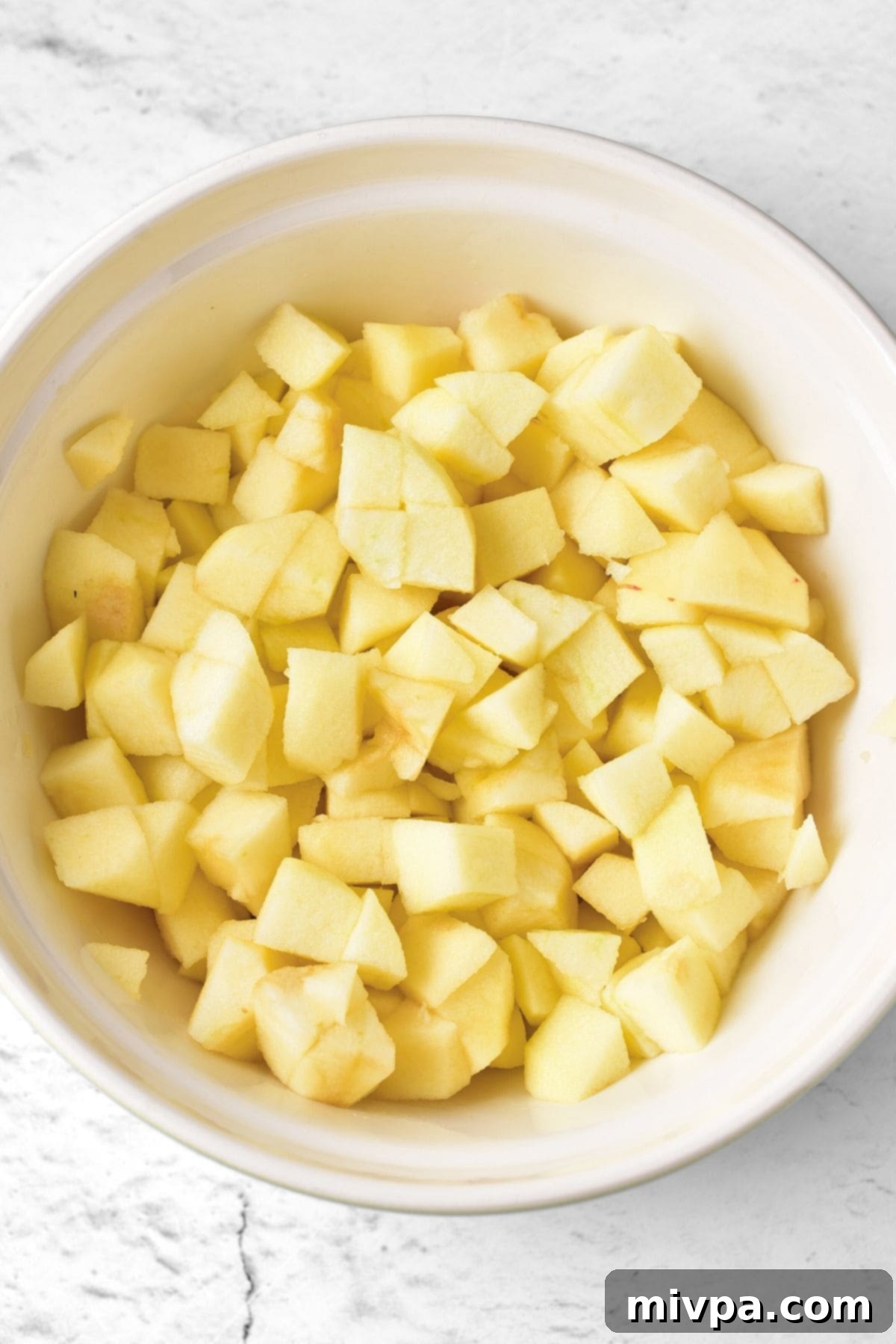 Freshly peeled, cored, and cubed apples neatly arranged in a white bowl, ready for the next step of making apple pie filling.