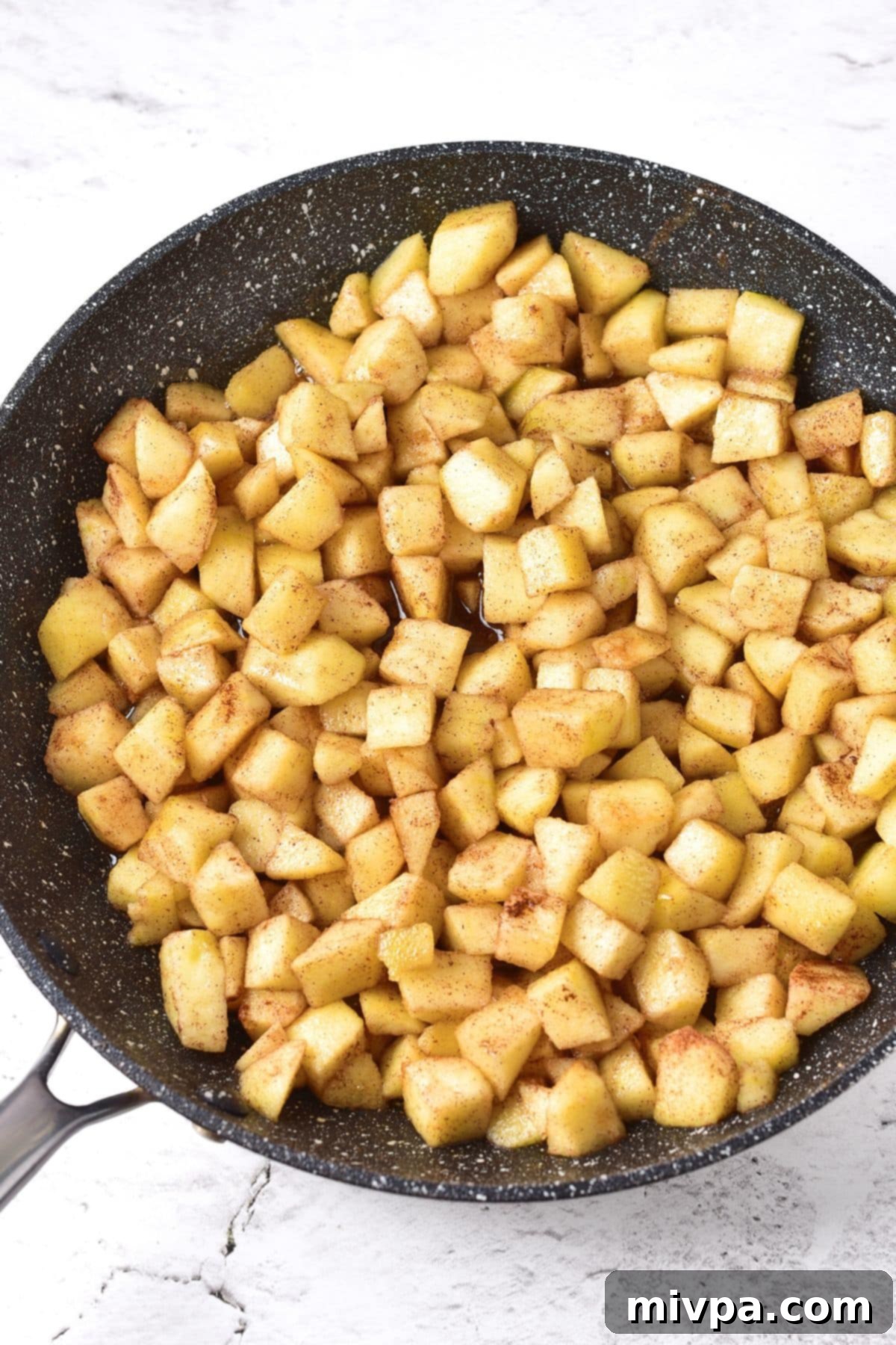 Cubed apples being cooked gently in a large nonstick skillet with melted dairy-free butter, starting the process of softening.