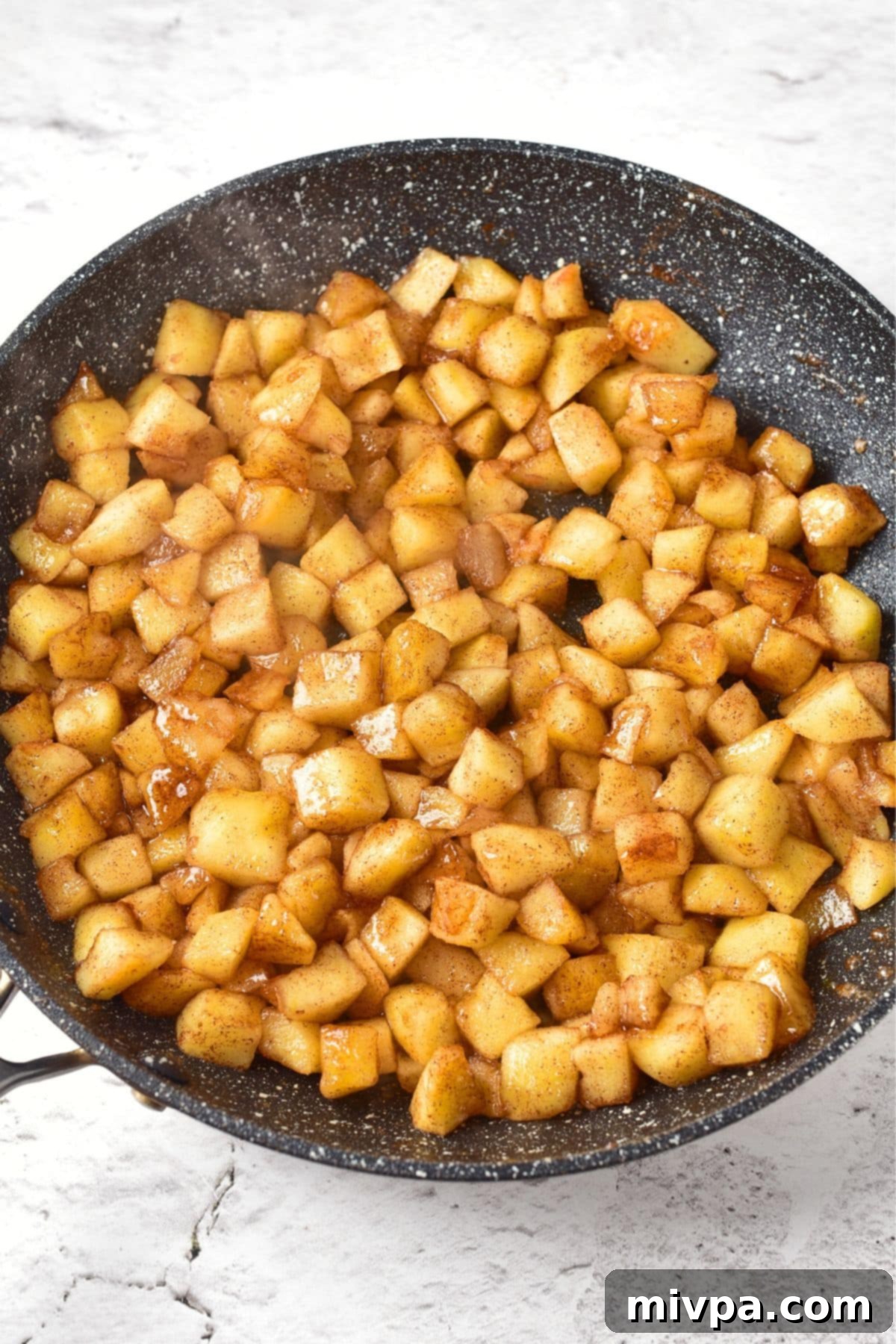 Cooked apple cubes shimmering in their own juices and melted butter within a skillet, appearing soft and tender after gentle cooking.