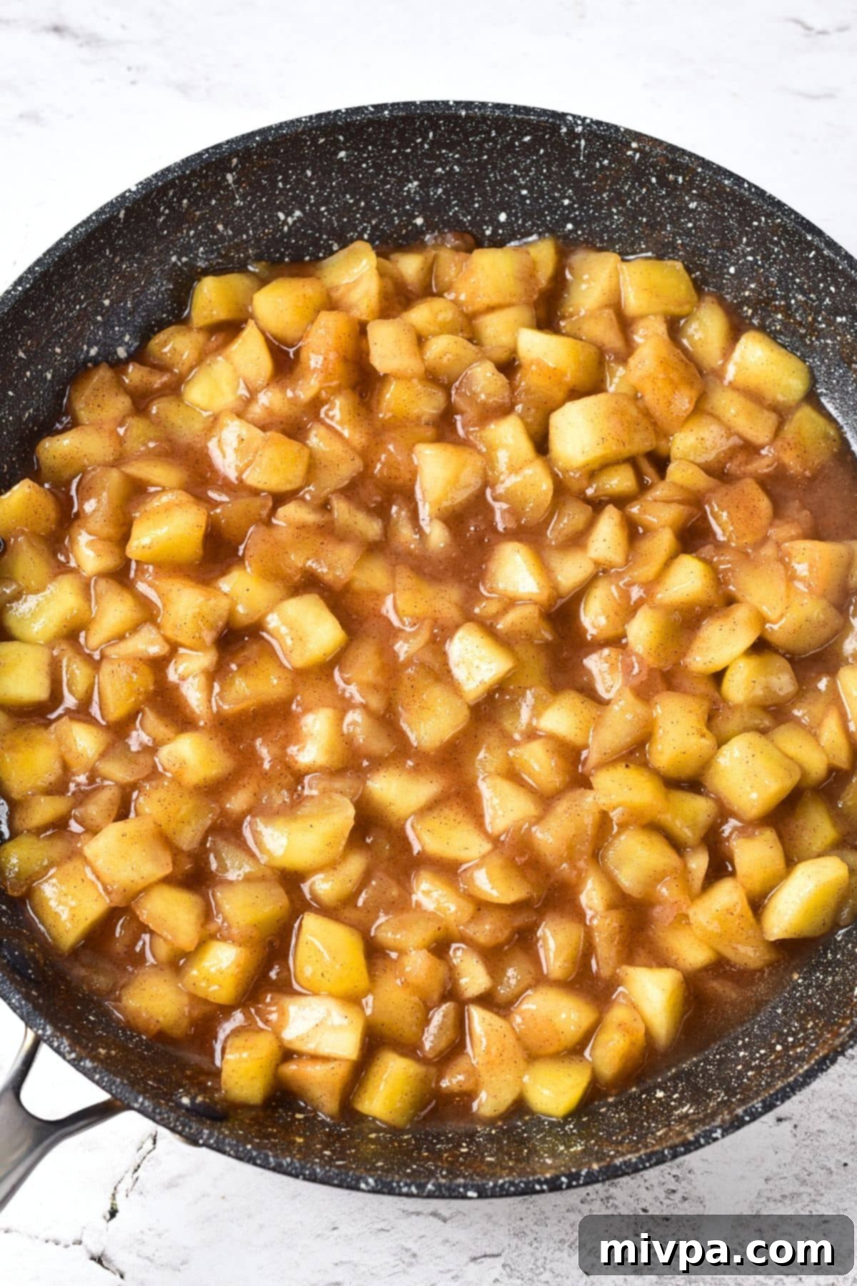 The apple pie filling in the skillet, now perfectly thickened and glossy after the addition of cornstarch slurry, ready for use.