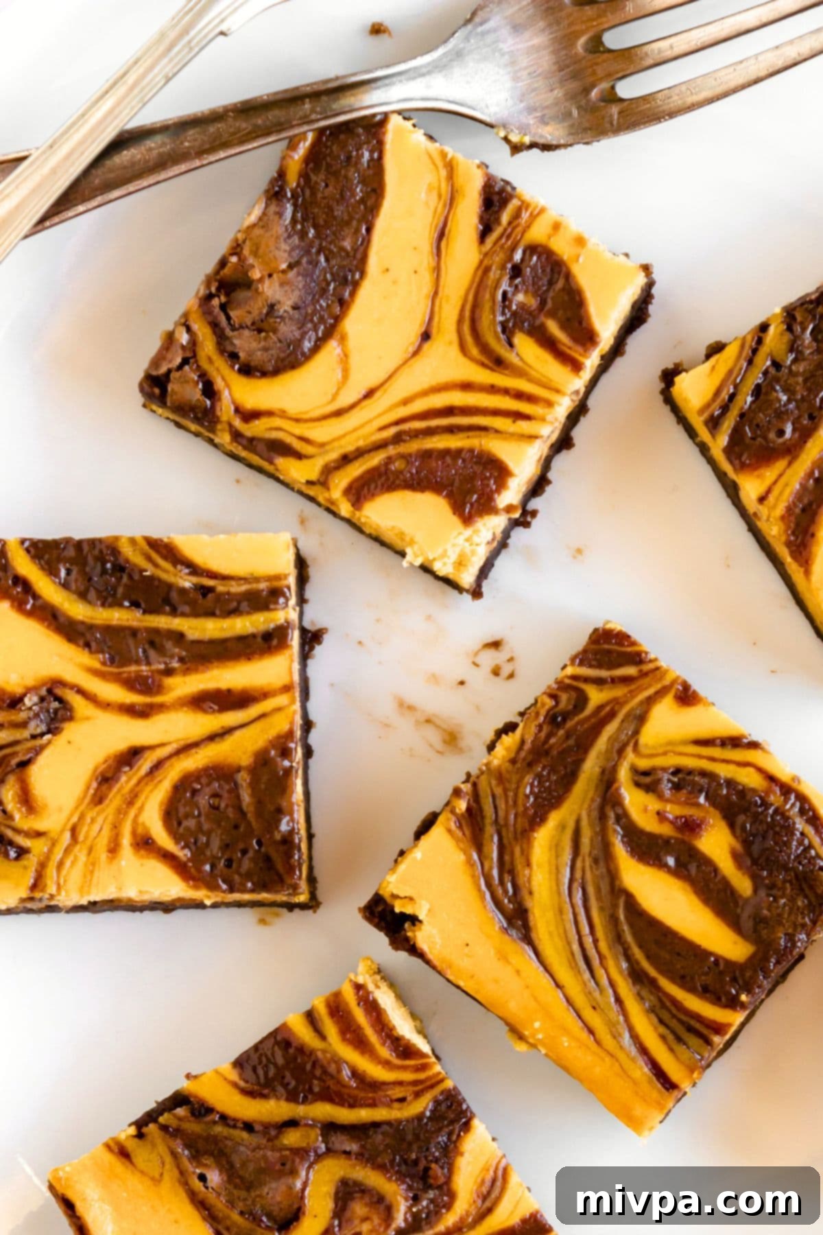 Cheesecake Pumpkin Brownies for Fall Top down view of freshly baked cheesecake pumpkin brownies cooling on parchment paper.