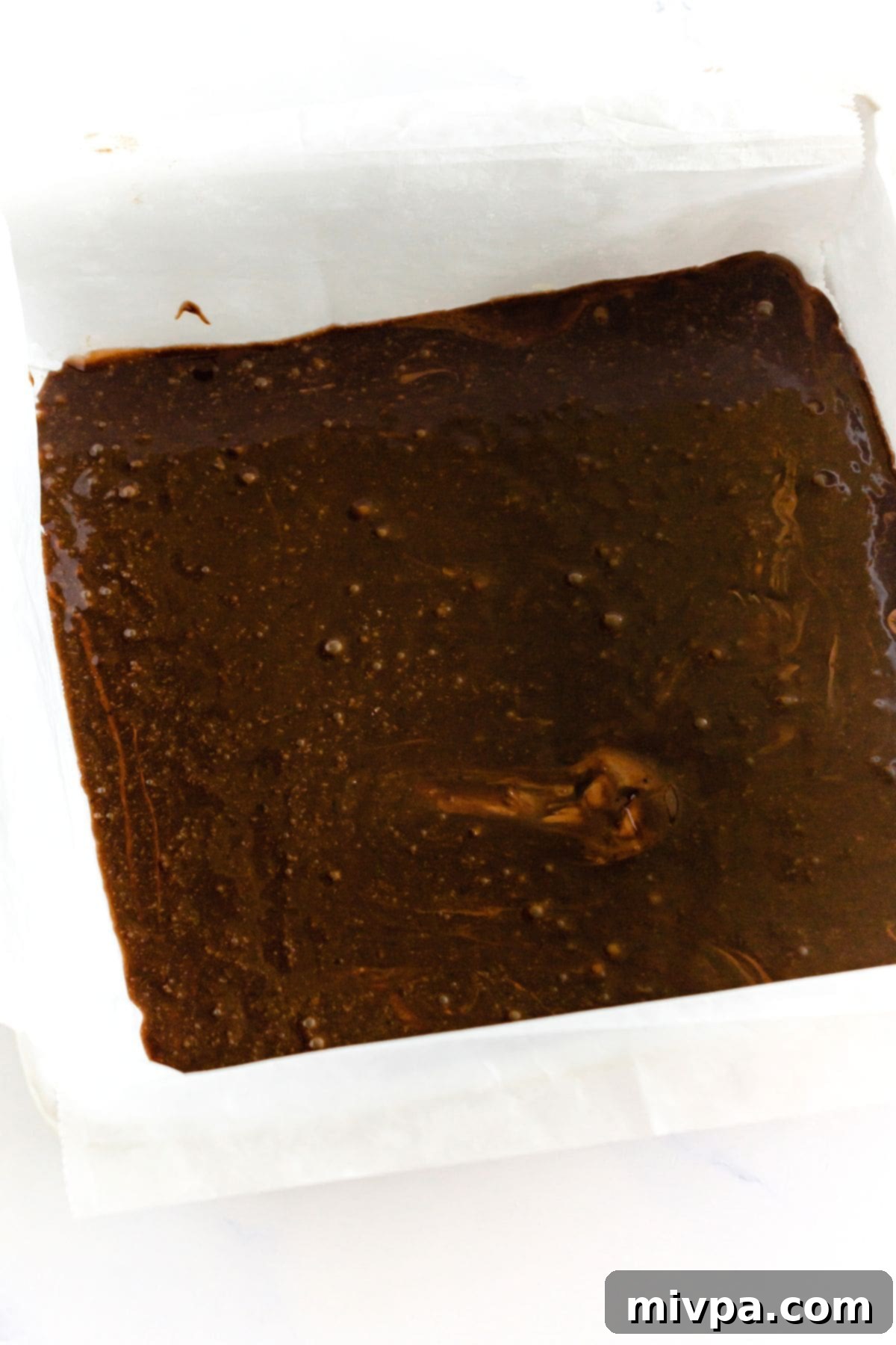 Pumpkin Cheesecake Brownie Recipe Base Layer Smooth, liquid brownie batter spread evenly in a parchment-lined baking sheet, forming the base layer.
