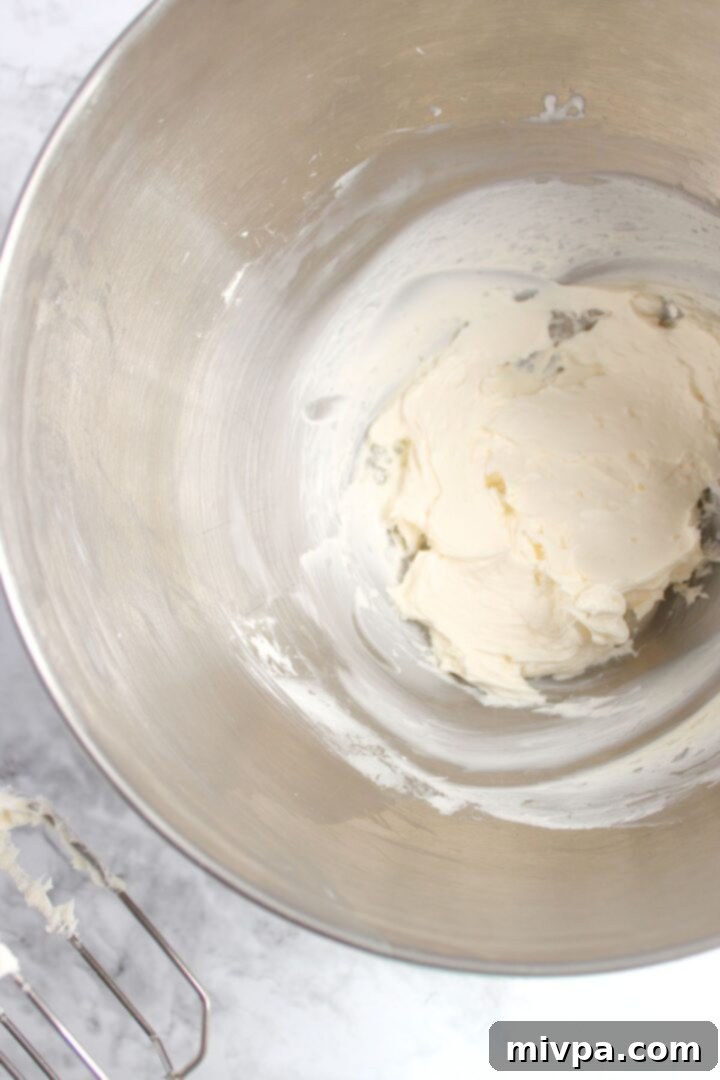 Beating cream cheese until smooth in a mixing bowl using a hand mixer.