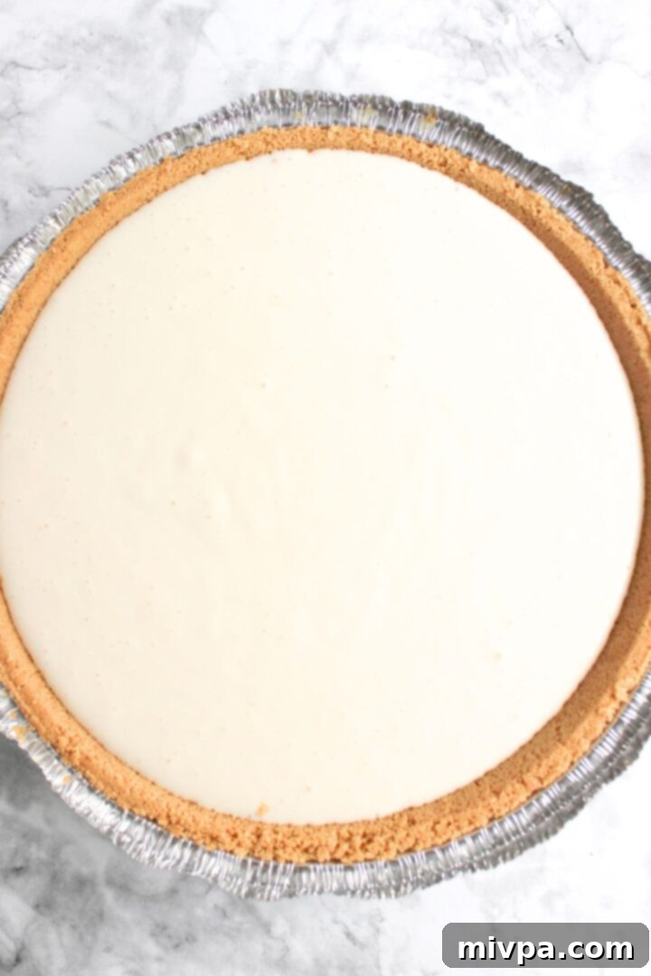 Unbaked cheesecake filling poured into a graham cracker crust, ready for the oven.
